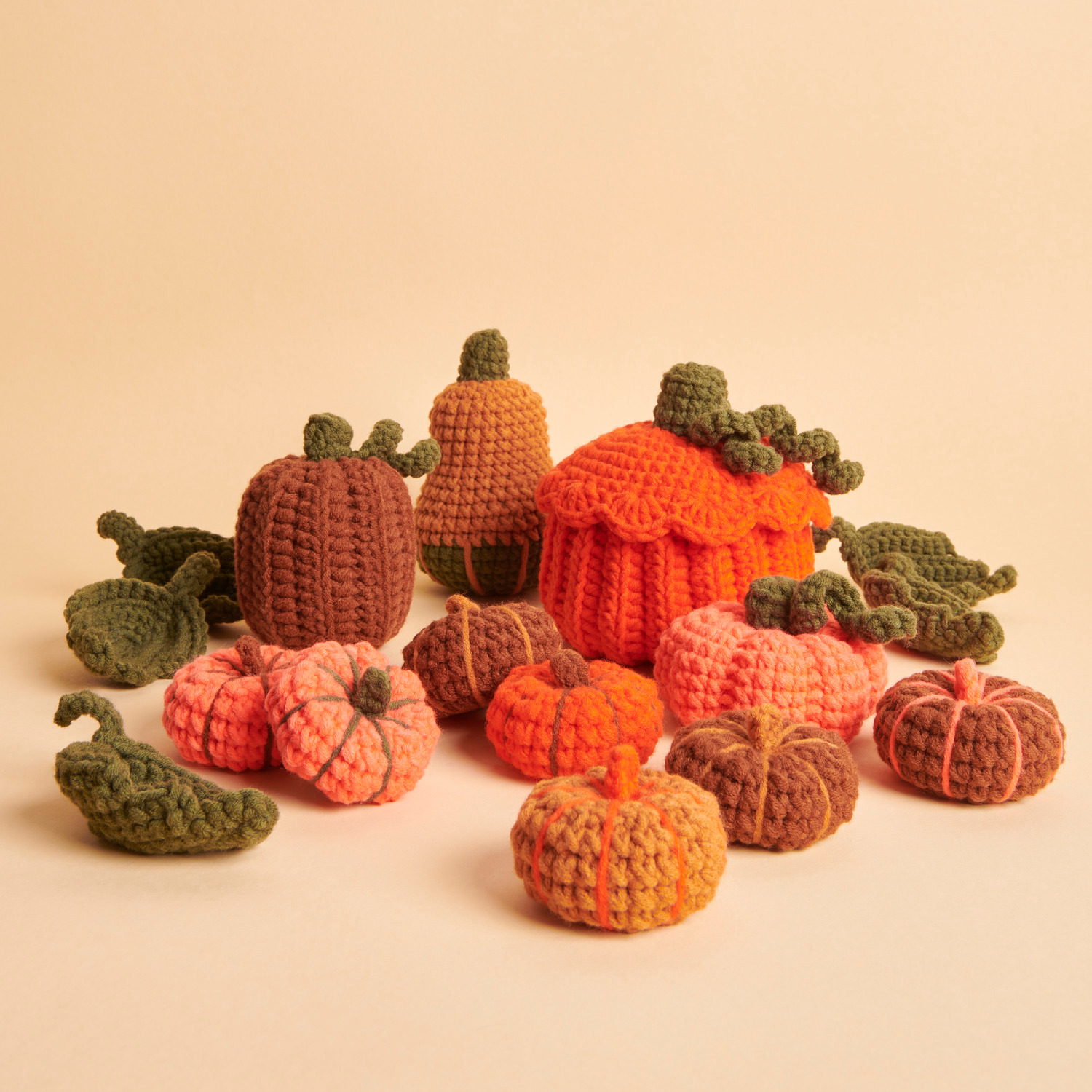 Häkelset Pumpkins: Verschiedene gehäkelte Kürbisse in Orange und Grün von Rico Design auf beigem Hintergrund.