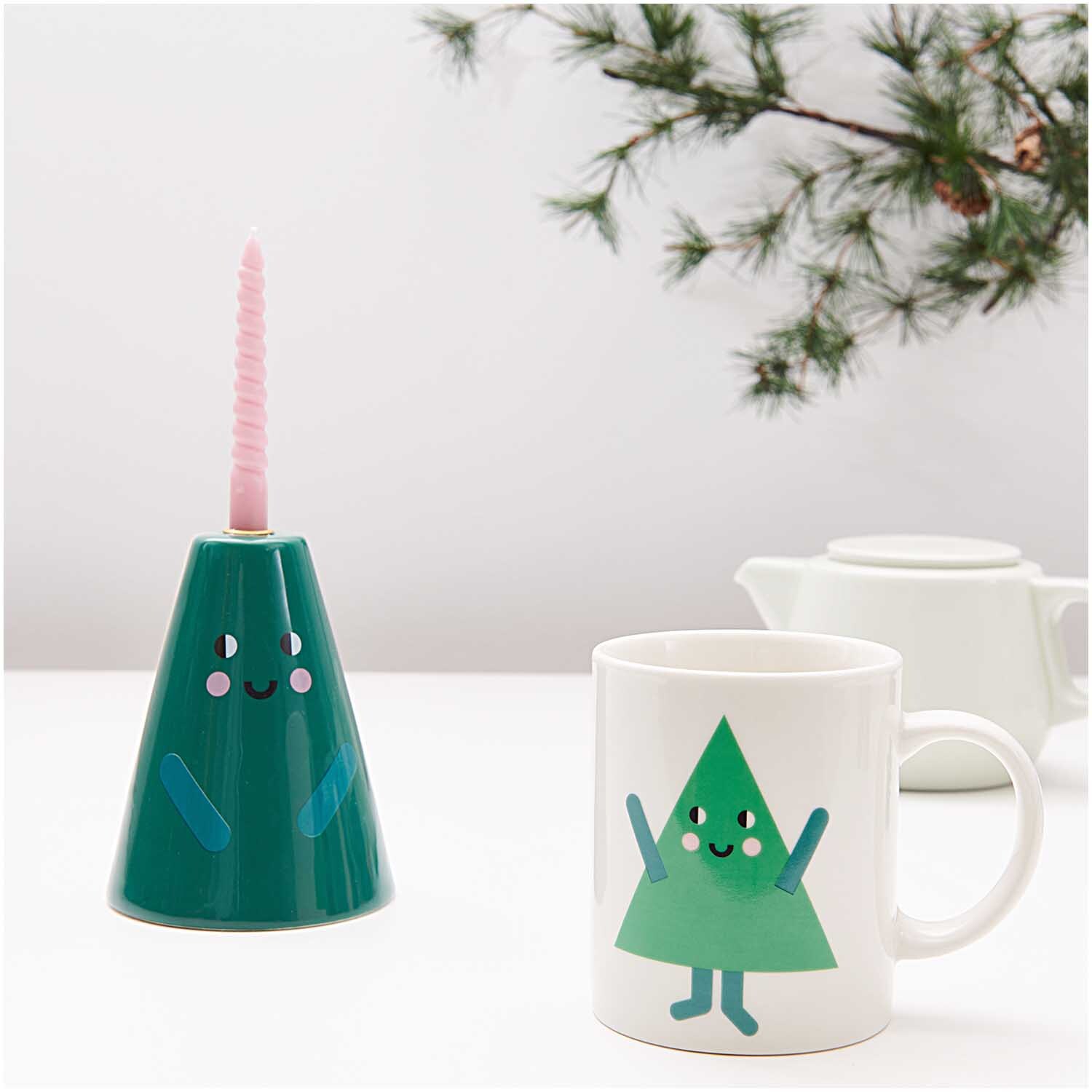 Porzellan Tasse Tanne 8x9,5cm mit fröhlichem Tannenbaum-Design, neben einem grünen Kerzenhalter.