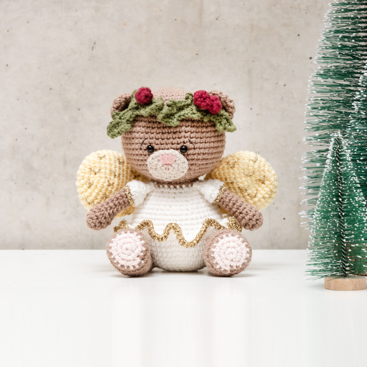 Häkelanleitung Ricorumi Teddyengel: Ein gehäkelter Teddyengel mit Flügeln und Blumenkranz, neben einem kleinen Tannenbaum.