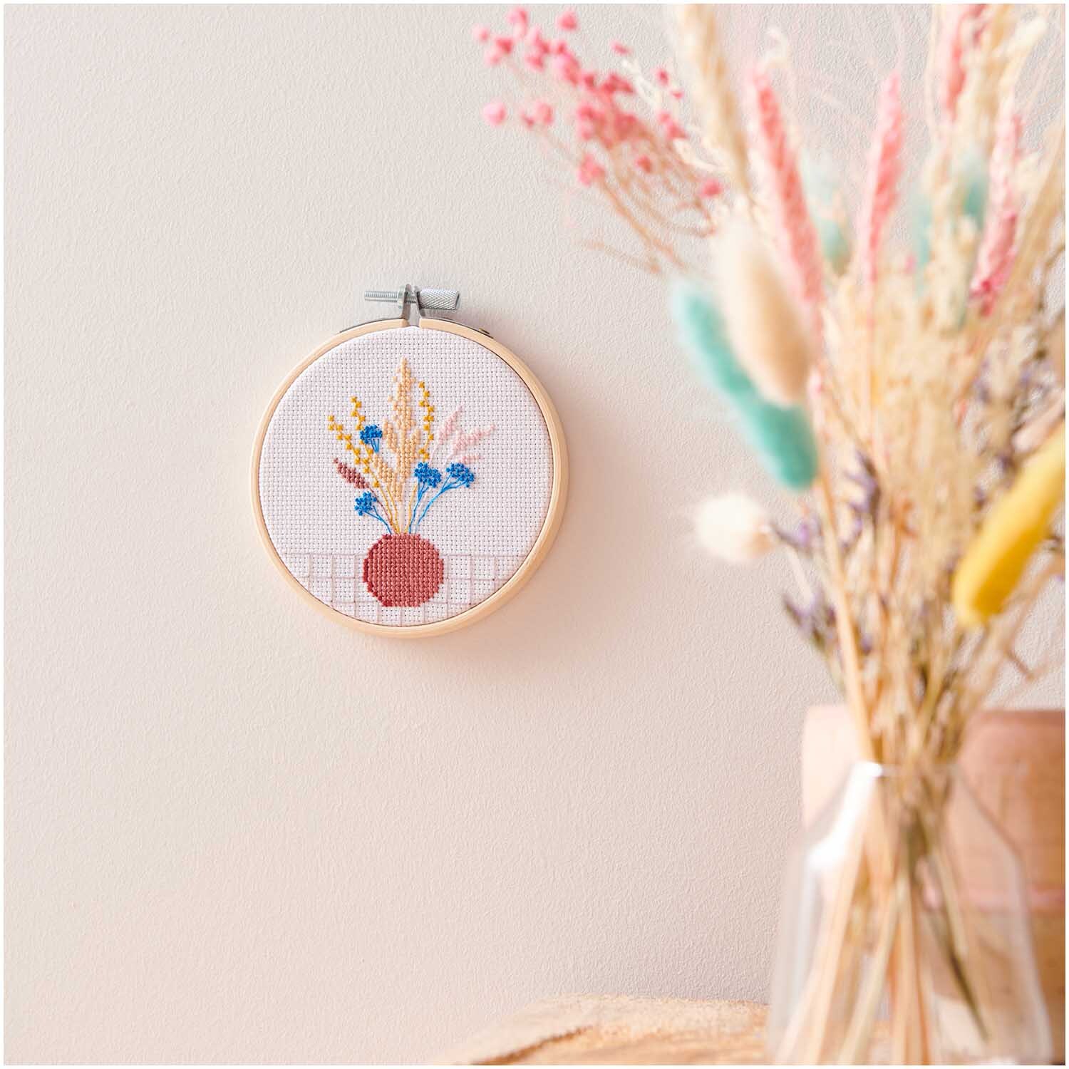 Stickpackung Mini Kit Trockenblumen Bild Ø 10cm zeigt bunte Blumen in einem Stickrahmen an der Wand.