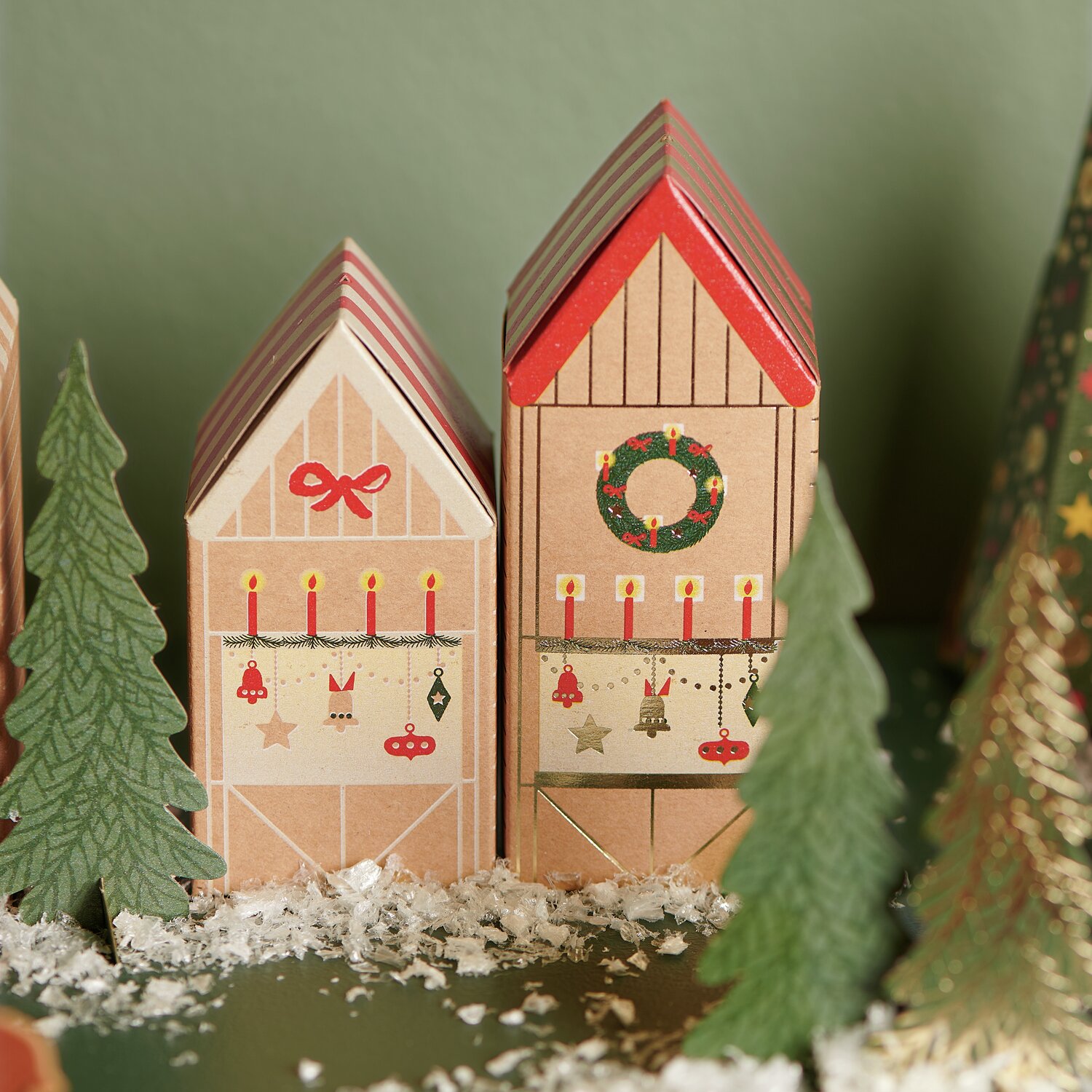 Adventskalender Bastelset: Zwei dekorative Häuschen mit roten Dächern, umgeben von Tannenbäumen.