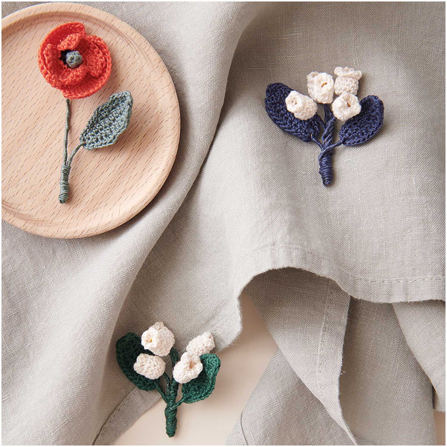 Essentials Crochet: Handgefertigte Häkelblumen auf cremefarbenem Stoff, ideal für kreative Projekte.