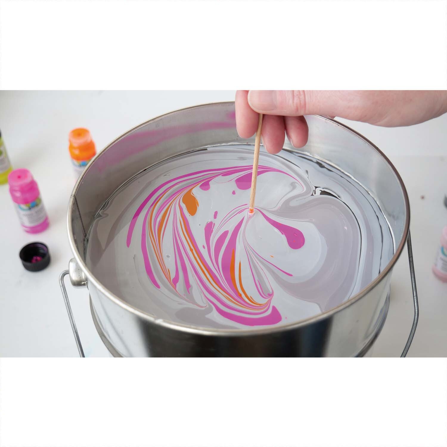 Magic Marble Marmorierfarben Set Love Neon 6x20ml: Eine Hand marmoriert Farben in einem Metallbehälter. Ideal für kreative Projekte.