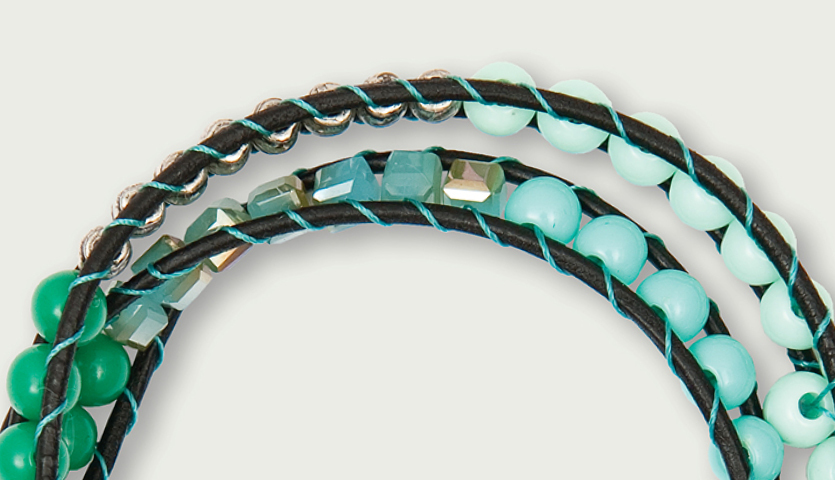 Anleitung Cooles Wickelarmband basteln: Detailaufnahme eines Armbands mit türkisfarbenen Perlen und schwarzem Lederband.