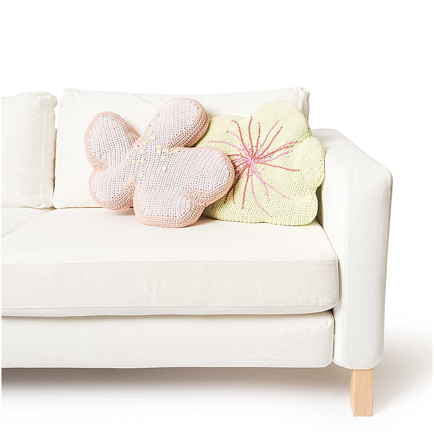 Fashion Jersey: Zwei gestrickte Blumenkissen in Pastellfarben auf einem weißen Sofa, ideal für stilvolle Wohnräume.