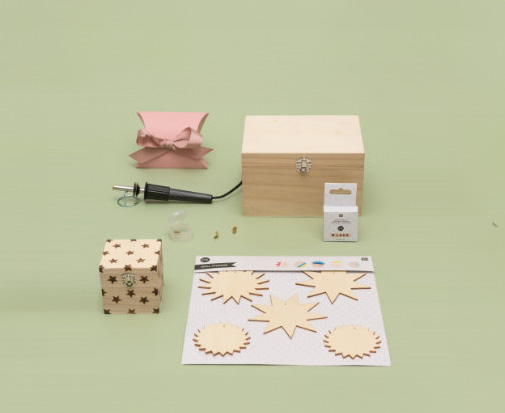 Ein Brandmalkolben mit Holzanhängern, einer großen Holzkiste und einer kleinen Holzkiste mit kleinen Sternen, sowie eine pinke Geschenkschachtel. Fotosetting grüne Wand.