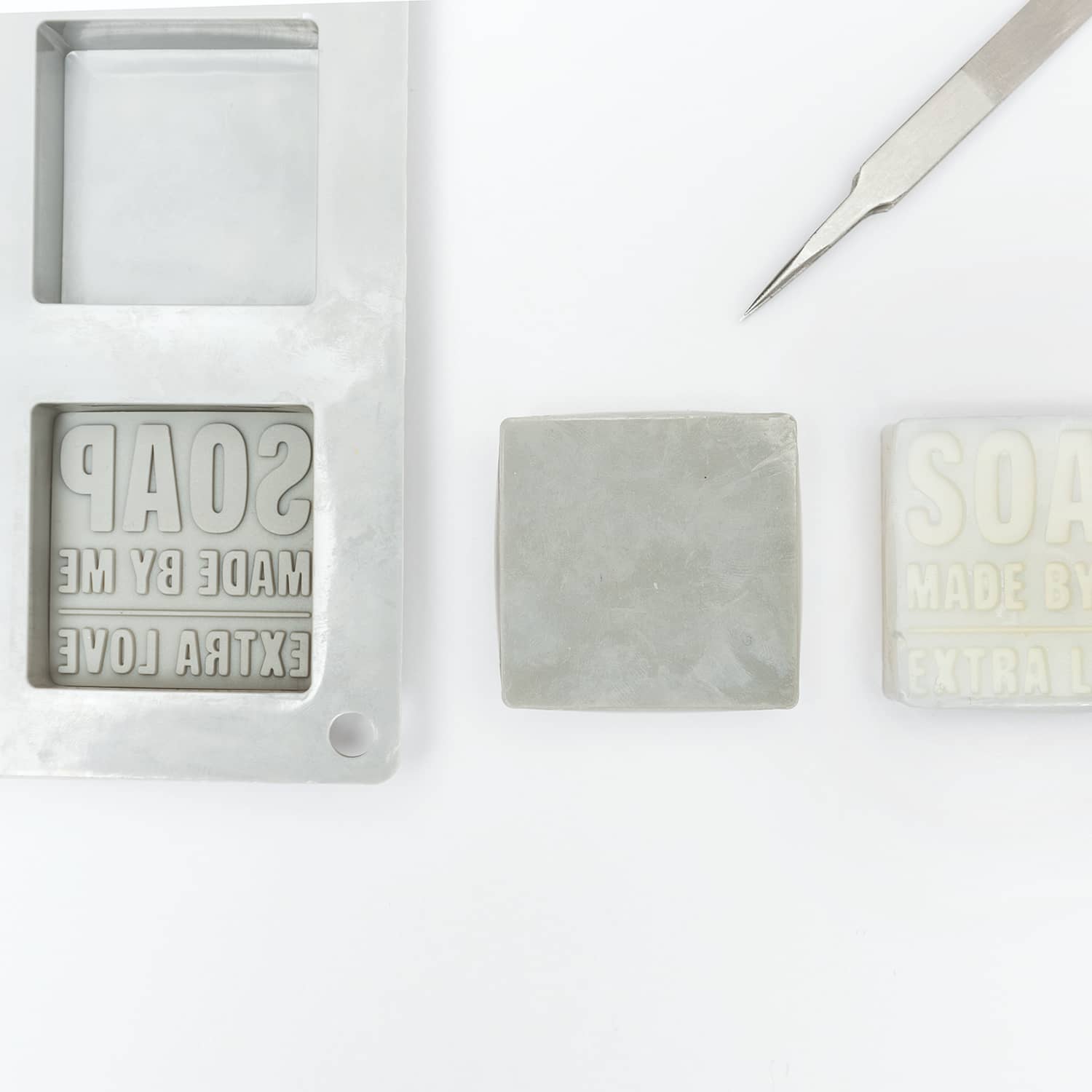 Eine Prägeform mit Schriftzug "Soap Made by Me" liegt in einer Seifengießform. Daneben ein Stück Seife mit genannter Prägung