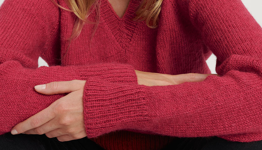 Strickanleitung Pullover aus weicher, roter Wolle mit V-Ausschnitt, getragen von einer Person.