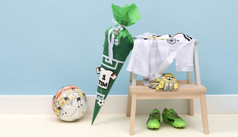 Bastelanleitung Fußball-Schultüte: Grüne Schultüte mit Fußballmotiv, umgeben von Fußball, Trikot und Sportschuhen.