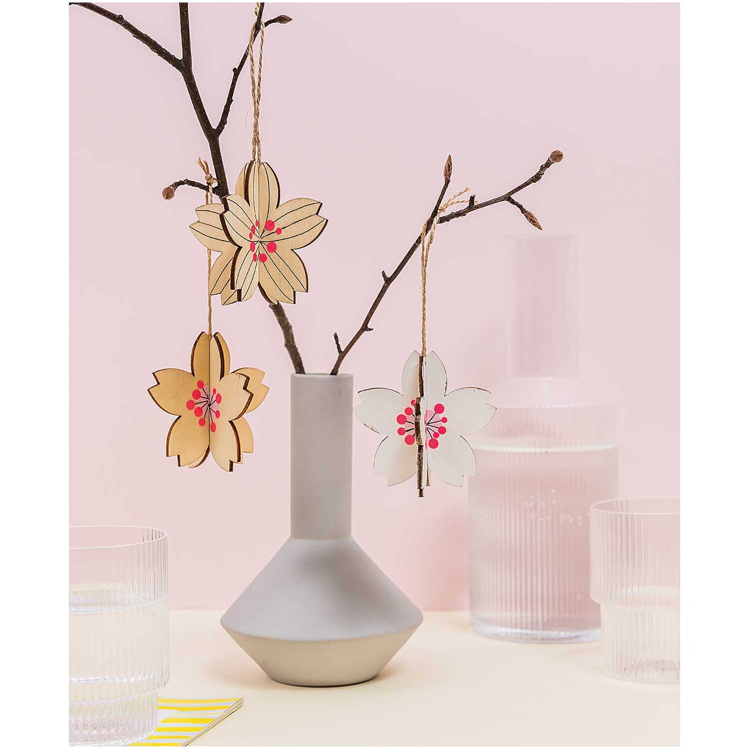 Steckblüten 6,5x6,5cm 3 Stück hängen an Zweigen in einer modernen Vase, umgeben von Glasgefäßen.