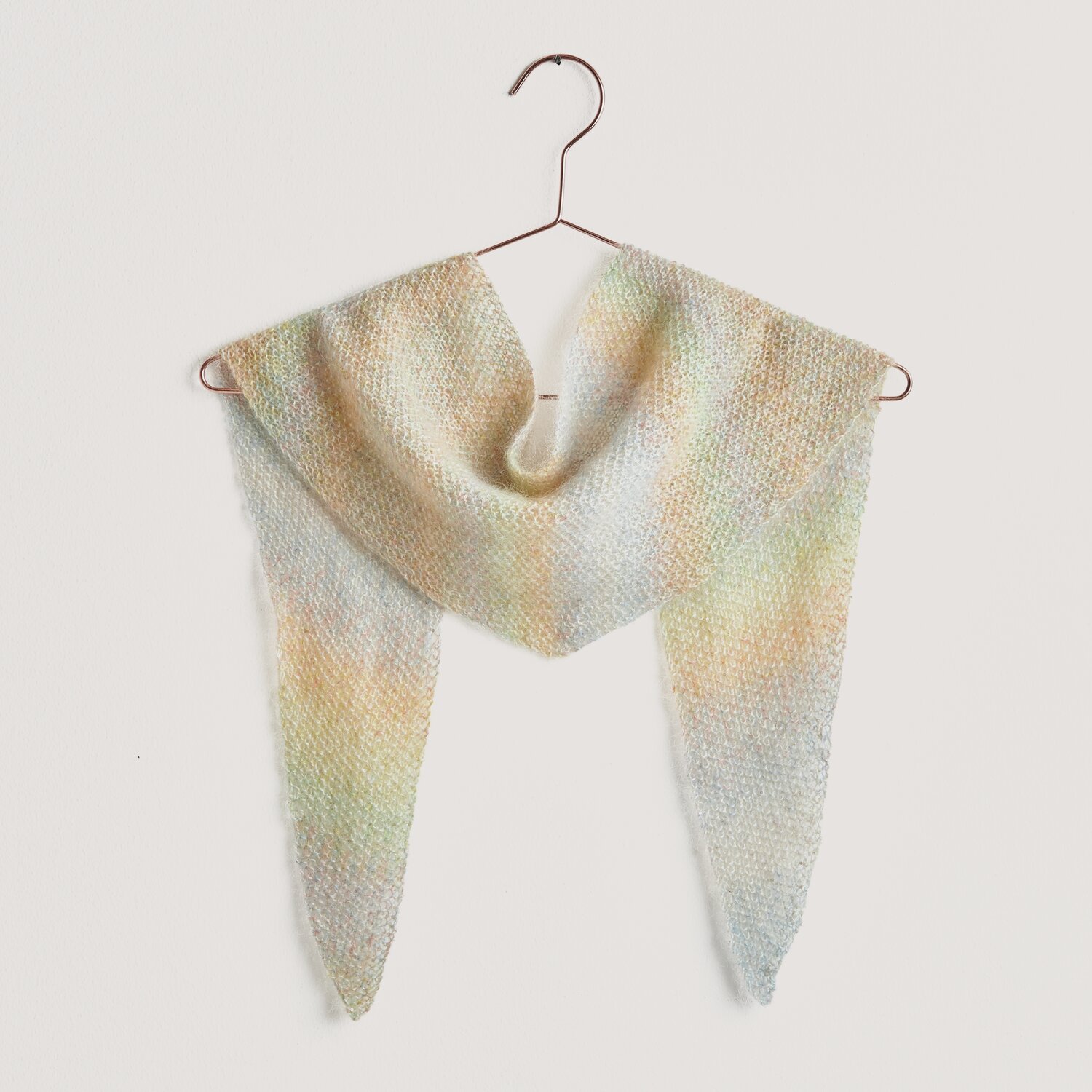 Strickset Mini-Dreieckstuch Modell 15b aus Lovewool No. 20, präsentiert in sanften Multicolor-Tönen, aufgehängt an einem Kleiderbügel.