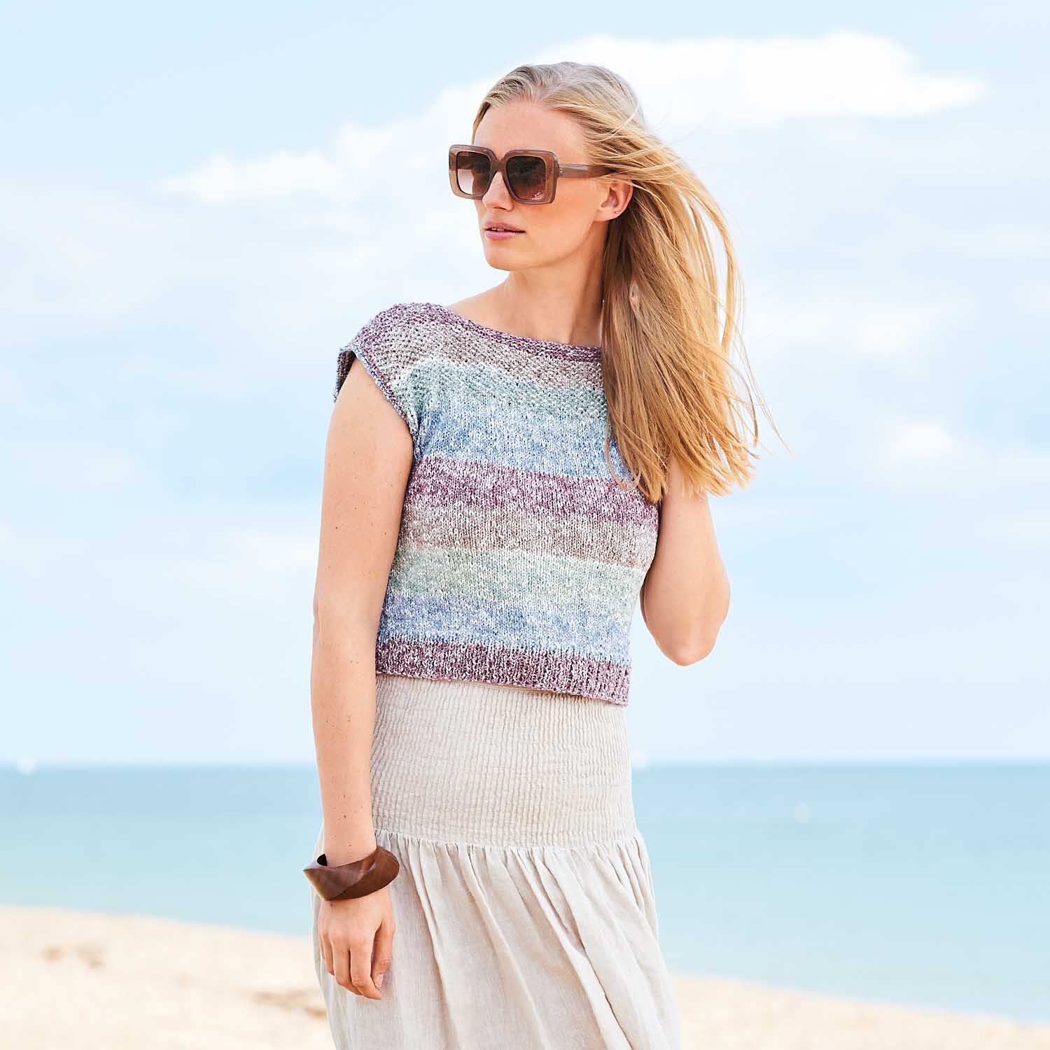 Strickanleitung Top aus Creative Cotton Stripes dk: Frau am Strand trägt ein gestreiftes, ärmelloses Oberteil mit Sonnenbrille und Armband.