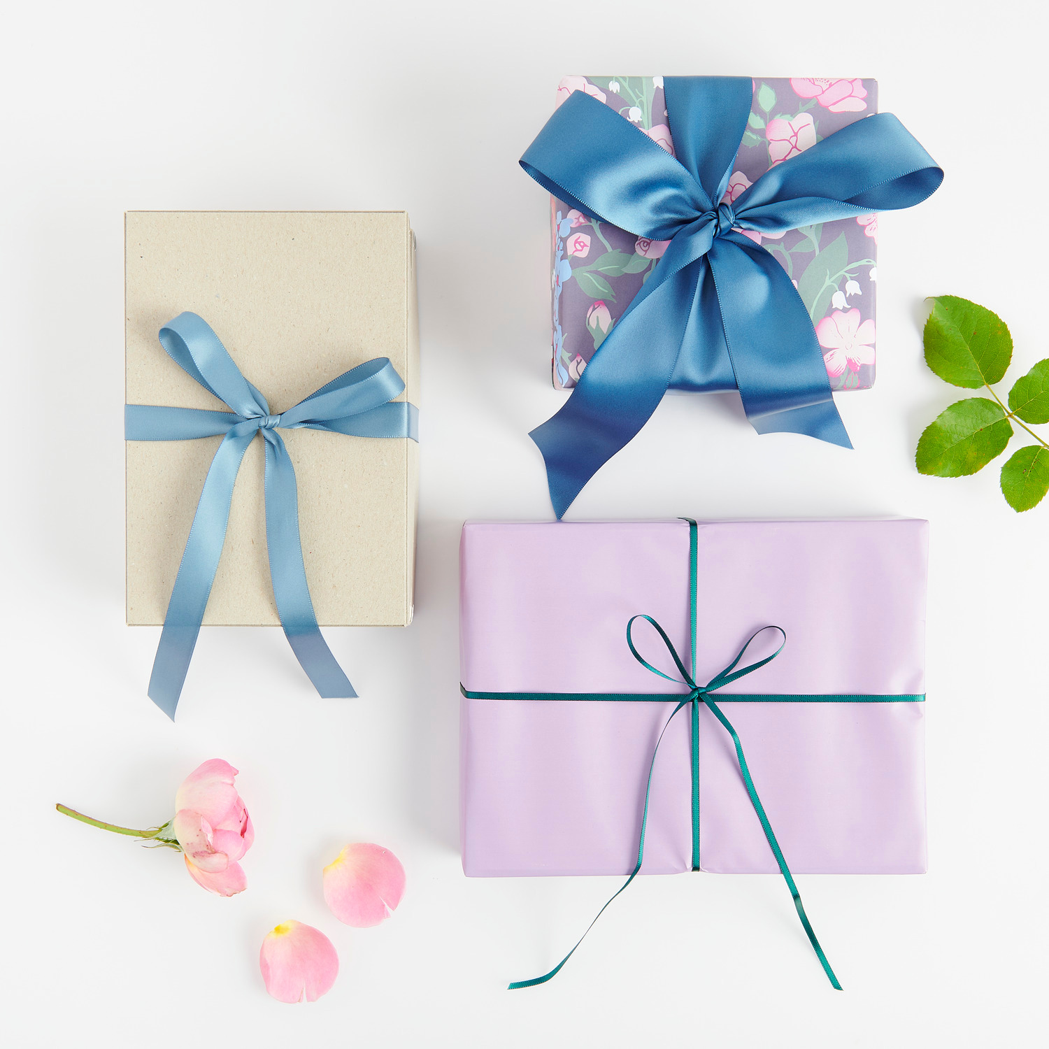 Paper Poetry Satinband 3mm 3m verziert drei Geschenke in Blau und Lila, umgeben von Blüten.