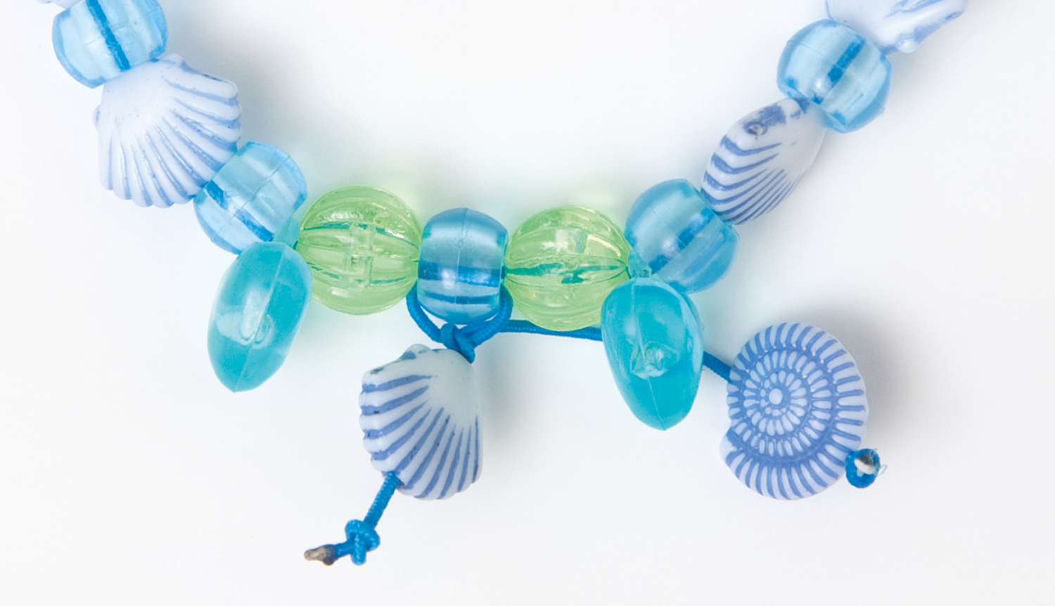 Anleitung DIY Perlenset: Bunte Muschel- und Glasperlen in Blau und Grün für Armbandgestaltung.