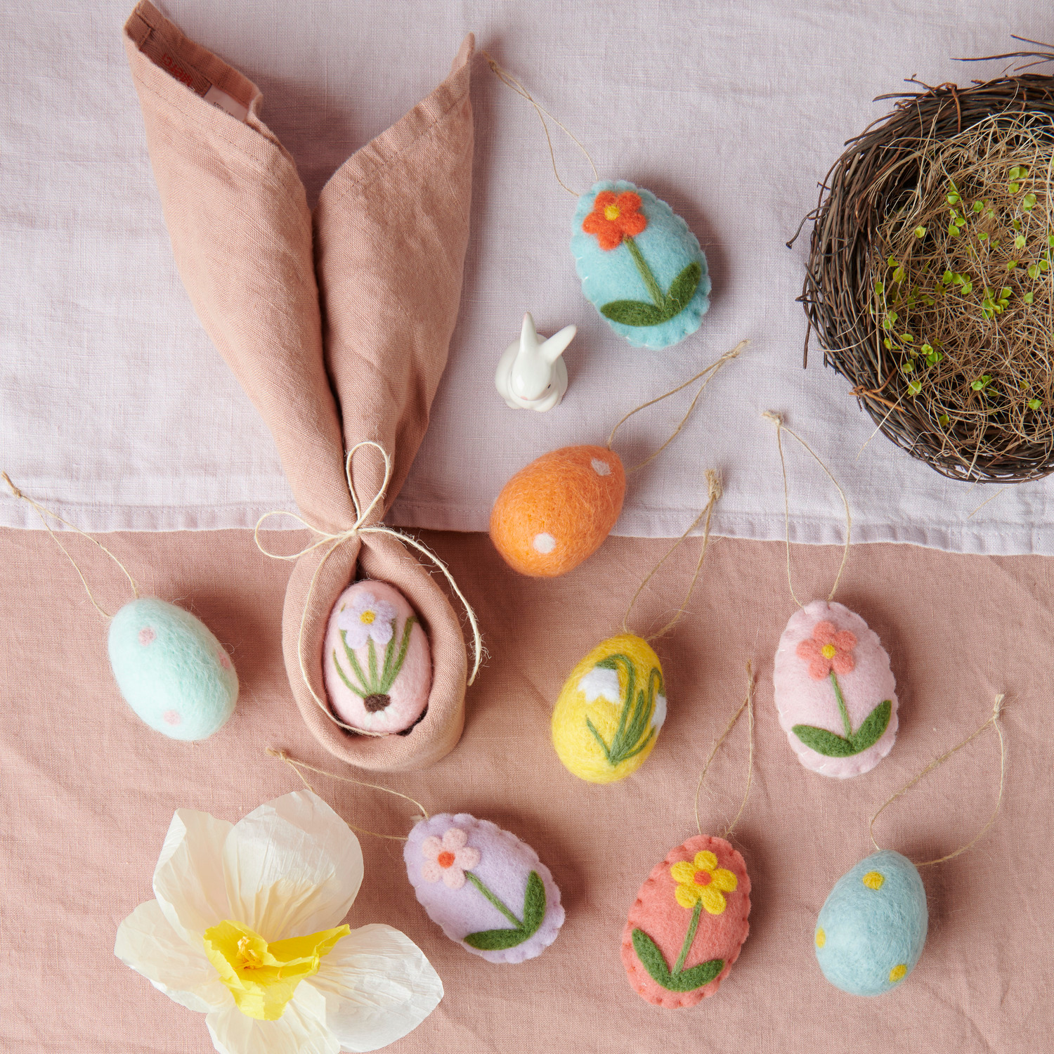 Aufhänger Filz-Eier Blumen: Bunte Filz-Eier mit Blumenmotiven, dekorativ arrangiert neben einem Naturnest auf einem Tisch.