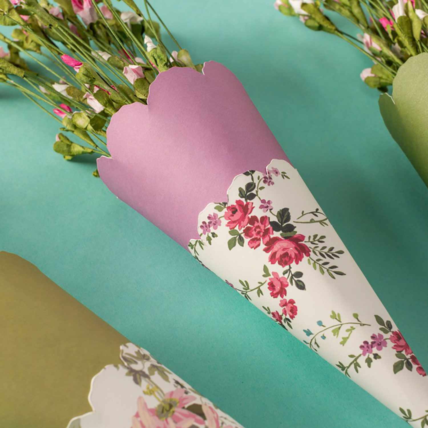 Maker Wavy Blade 31 Wellenförmige Klinge schneidet präzise florale Papierkegel mit Blumen auf türkisfarbenem Hintergrund.
