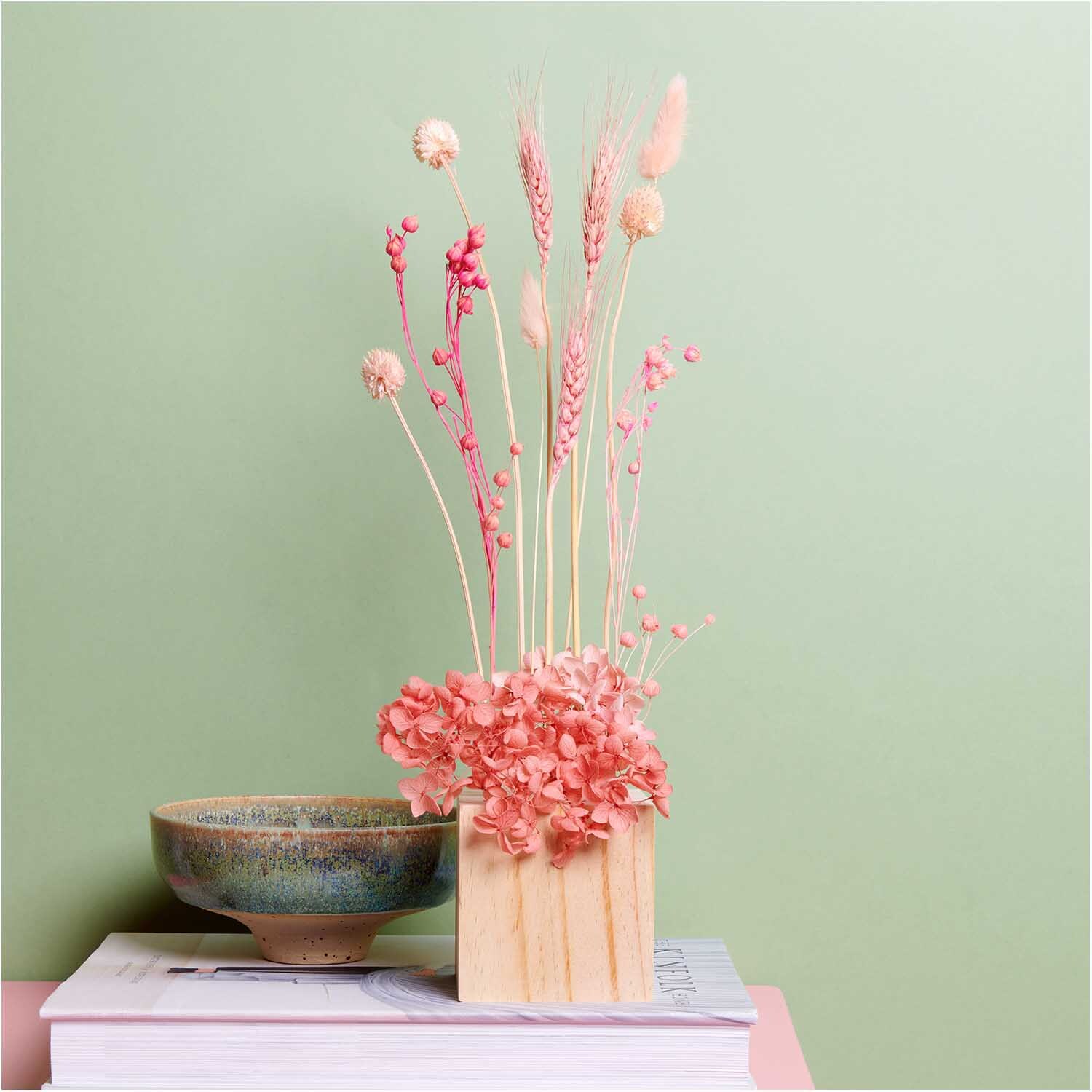 Getrockneter Weizen pink 60-70cm 50 Stück in Vase auf Tisch vor grünem Hintergrund, dekorativ arrangiert.