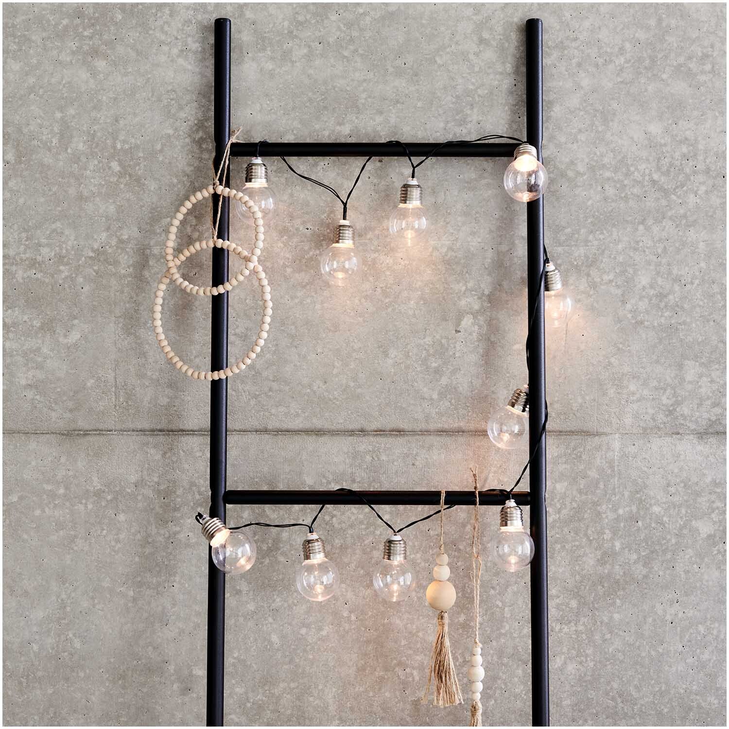 LED-Lichterkette Glühlampen 150cm von Rico Design, dekorativ an einer schwarzen Leiter aufgehängt, ideal für stimmungsvolle Beleuchtung.