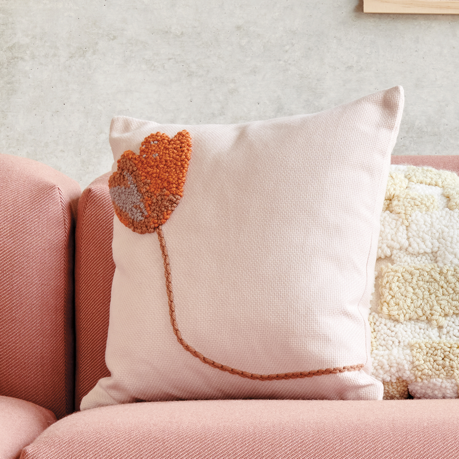 Punch Needle Anleitung Kissen mit Blumenmotiv: Ein dekoratives Kissen mit gesticktem Blumenmuster auf einem rosa Sofa.