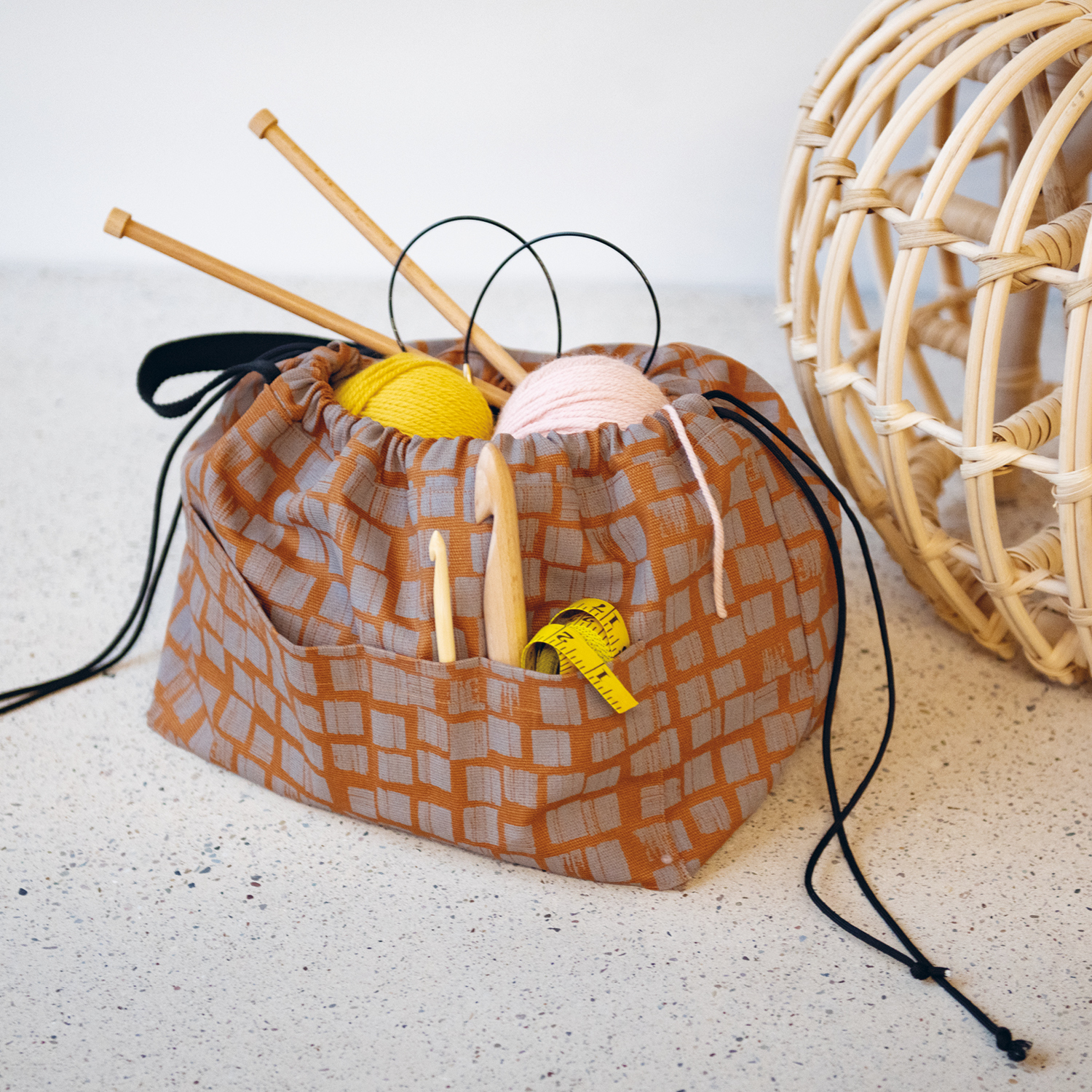Nähanleitung Handarbeitstasche: Eine gemusterte Tasche mit Stricknadeln, Wolle und Maßband auf hellem Untergrund.