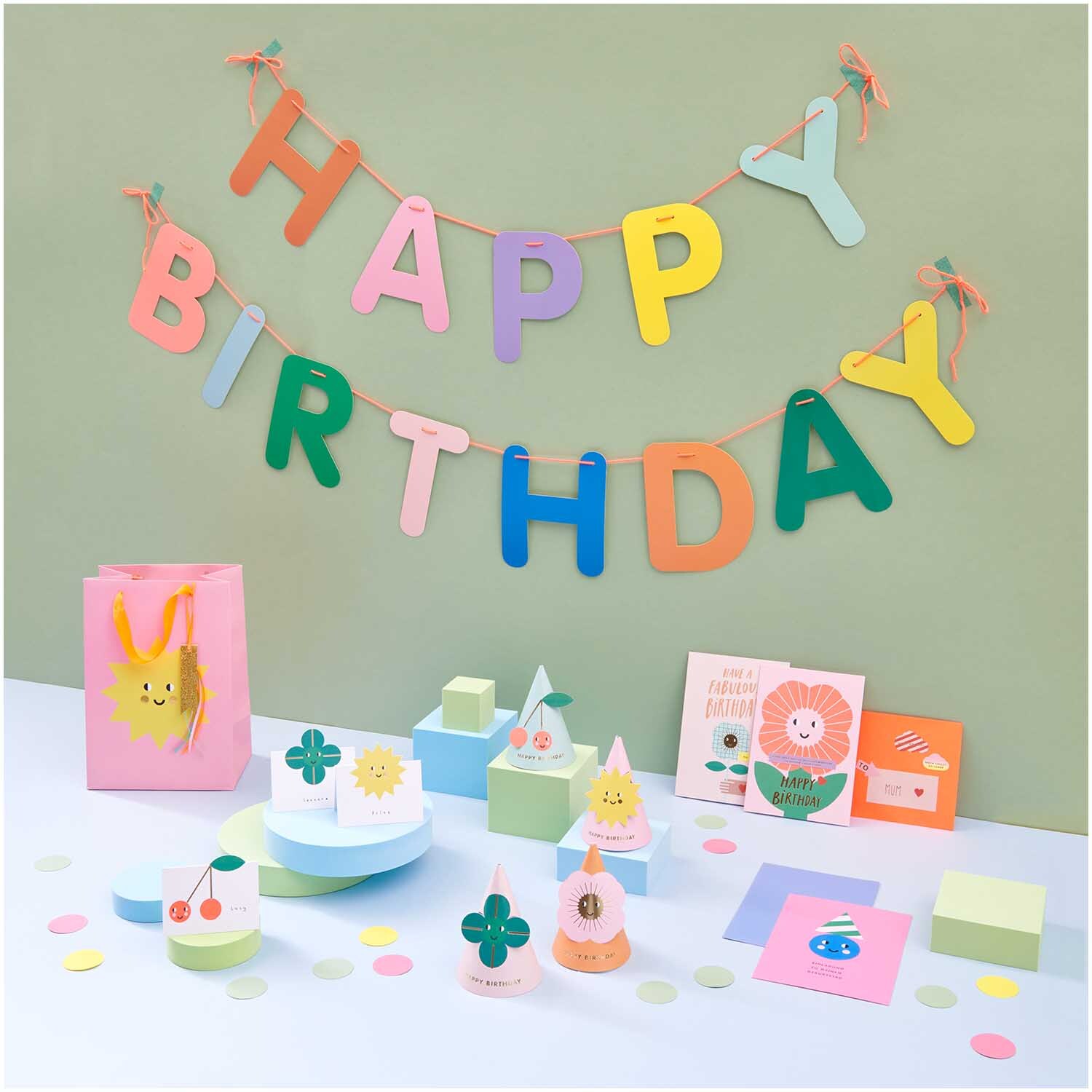 Paper Poetry Girlande Happy Birthday 5m von Rico Design in bunten Farben, dekoriert mit Partyartikeln und Geschenken auf einem Tisch.