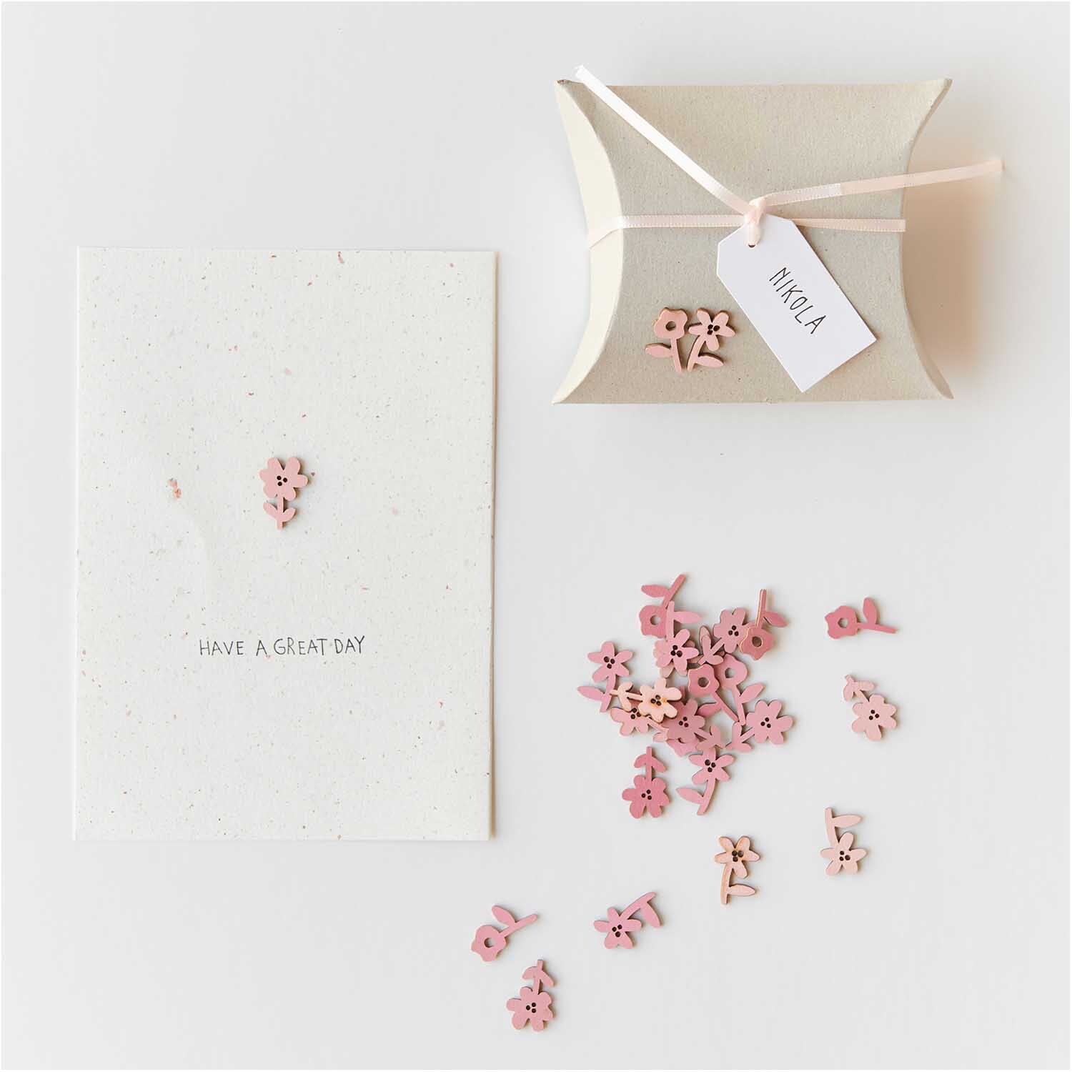 Holzstreu Blume 48 Stück in Rosa Mix von Rico Design, dekorativ arrangiert neben einer Karte und Geschenkbox.