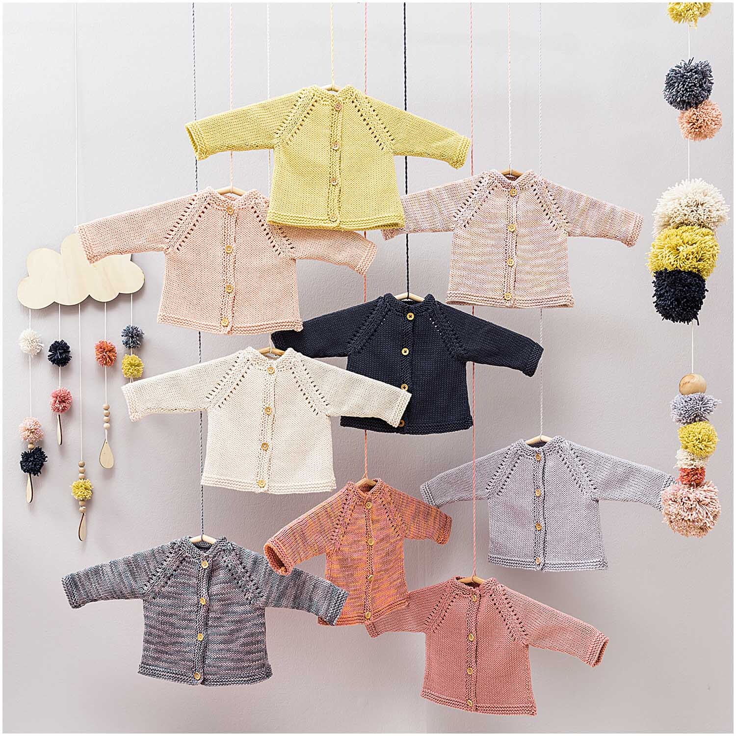 Rico Baby Cotton Soft Print dk: Strickjacken in sanften Pastelltönen hängen dekorativ an einer Wand.