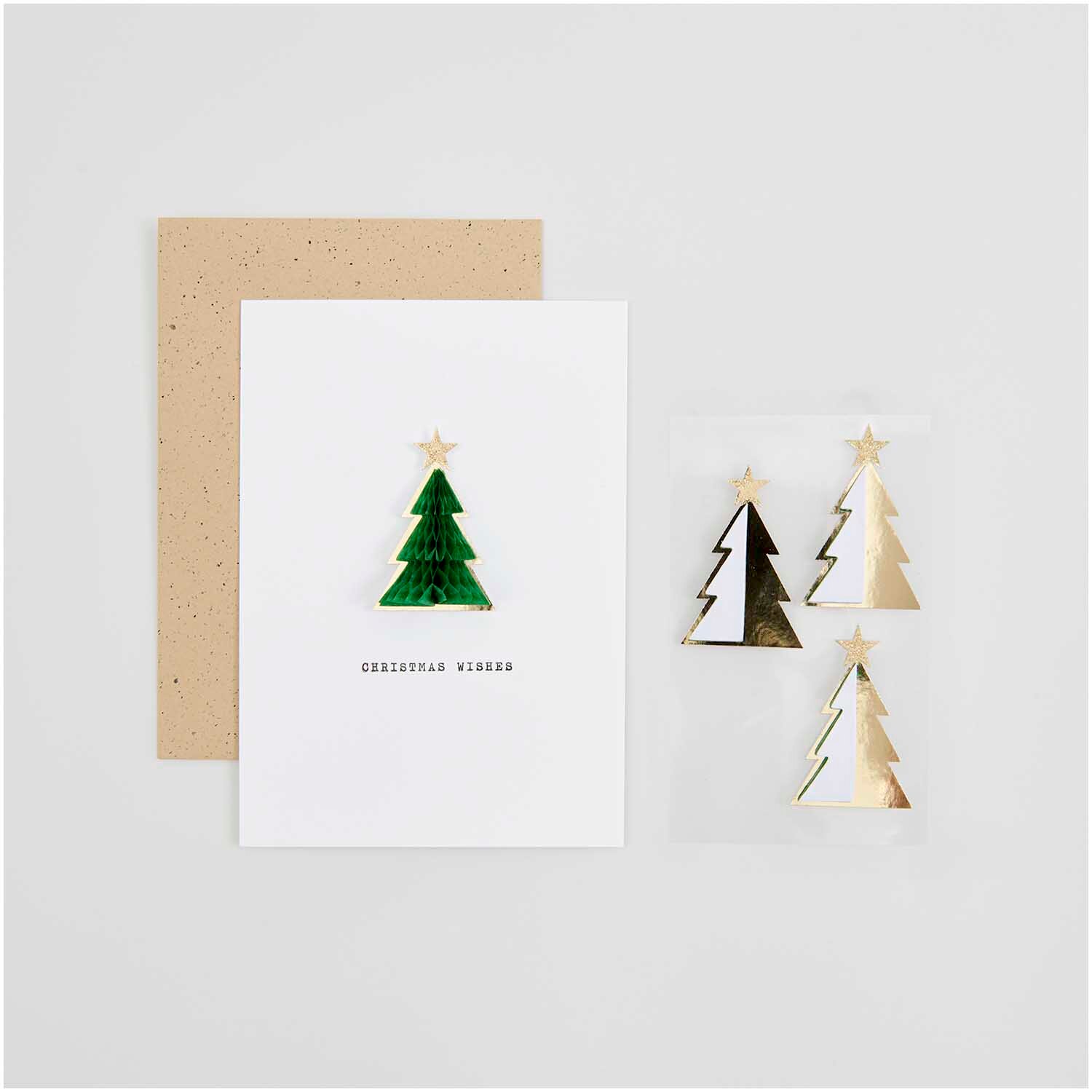 Paper Poetry Wabenpapiersticker Tannen auf einer Karte mit Umschlag, verziert mit goldenen und grünen Tannenbaumstickern von Rico Design.