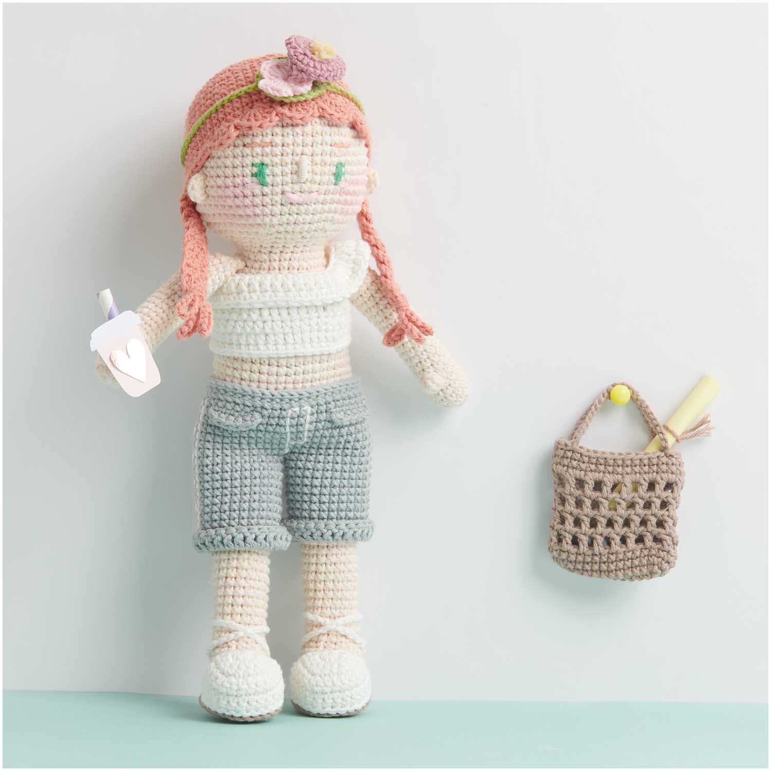 Creative Ricorumi dk: Gehäkelte Puppe mit rosa Haaren und blauer Shorts, neben einer kleinen Tasche.