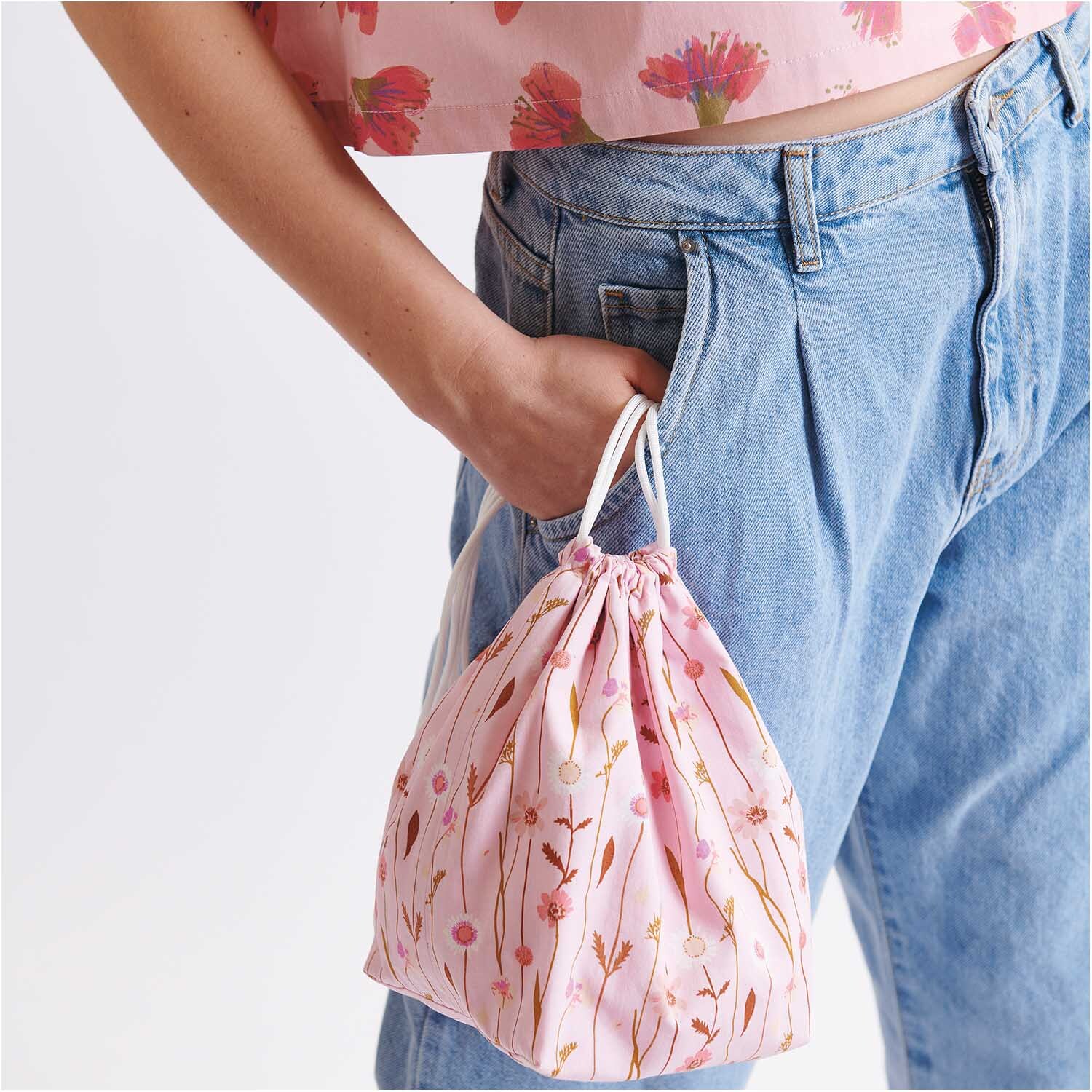 Stoffabschnitt Druckstoff Wildblumen rosa 50x140cm: Frau hält rosa Beutel mit Wildblumenmuster, trägt Jeans und passendes Oberteil.