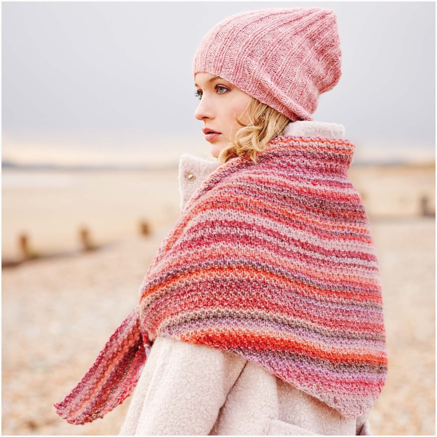 Creative Melange chunky: Frau mit gestricktem Schal und Mütze in Rosa-Blau, am Strand stehend.