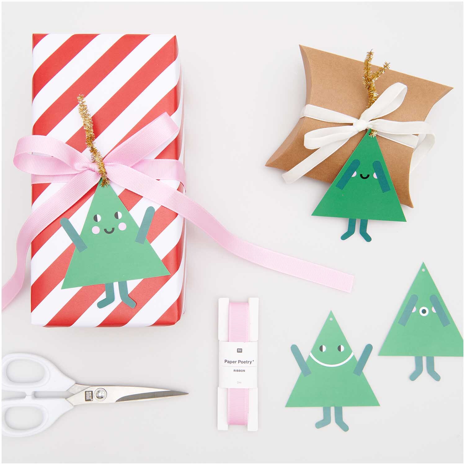 Paper Poetry Geschenkanhänger Tannen, 8 Stück, von Rico Design. Zwei Geschenke mit grünen Tannenbaum-Anhängern, rosa Schleifen und Schere.