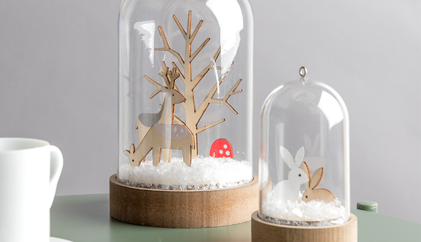 Bastelanleitung Dekohauben: Zwei Glasglocken mit Holzfiguren von Reh und Hase auf Schneebett.