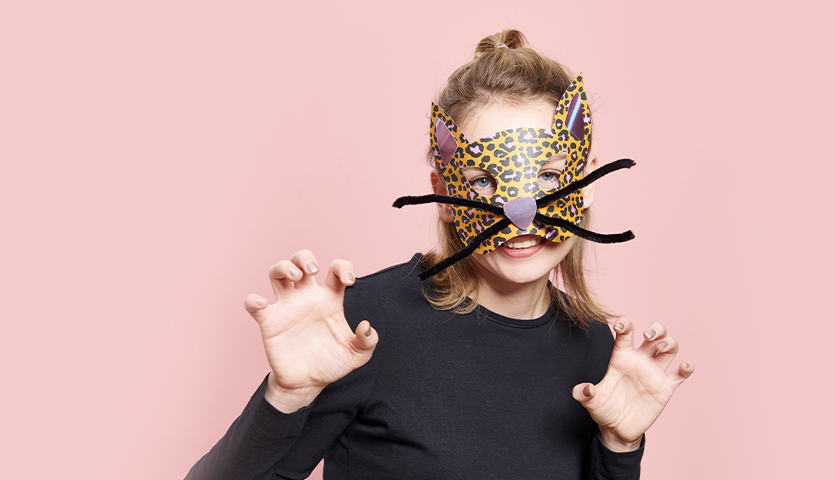 Bastelanleitung coole Leomaske: Frau mit Leopardenmaske und schwarzen Schnurrhaaren vor rosa Hintergrund.