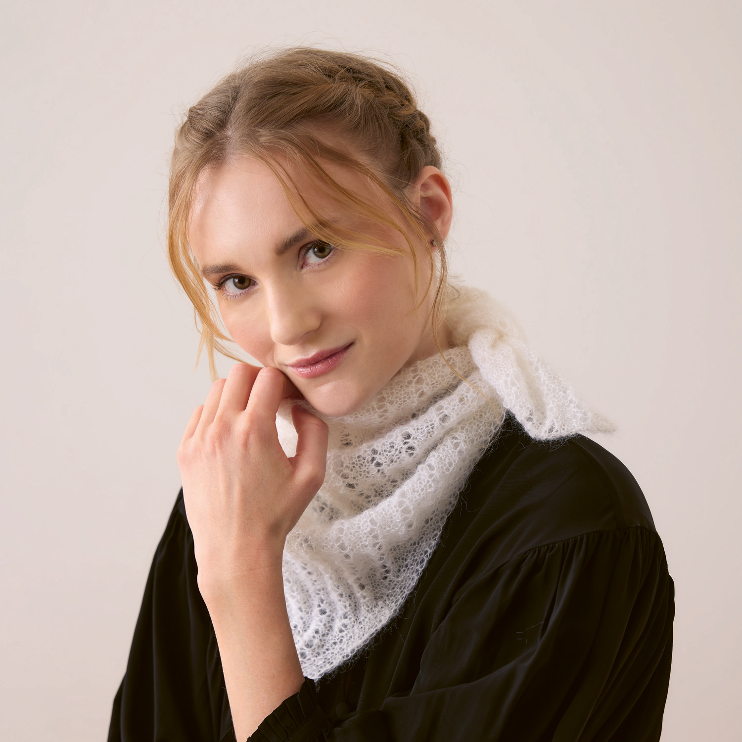 Essentials Super Kid Mohair Loves Silk Strickset zeigt ein weißes Dreieckstuch von Rico Design, getragen von einer Frau in schwarzer Kleidung.