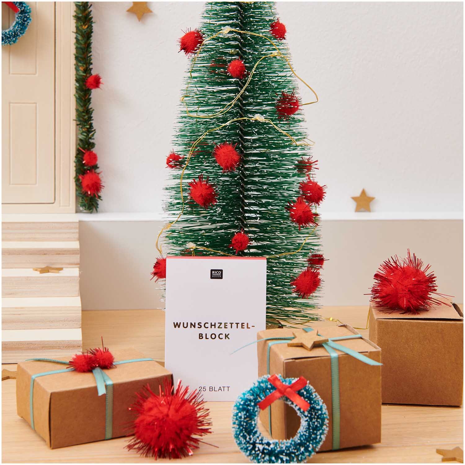 Paper Poetry Wunschzettelblock A8 vor einem festlich dekorierten Weihnachtsbaum mit Geschenken.
