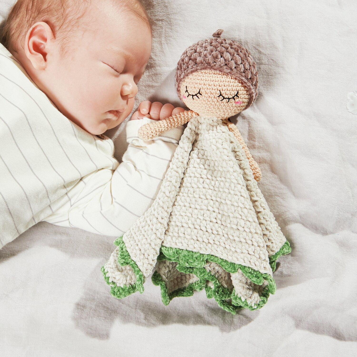 Ricorumi Baby Blankies Nilli Nilli: Ein Baby schläft neben einer gehäkelten Puppe mit grünem Rand, von Rico Design.