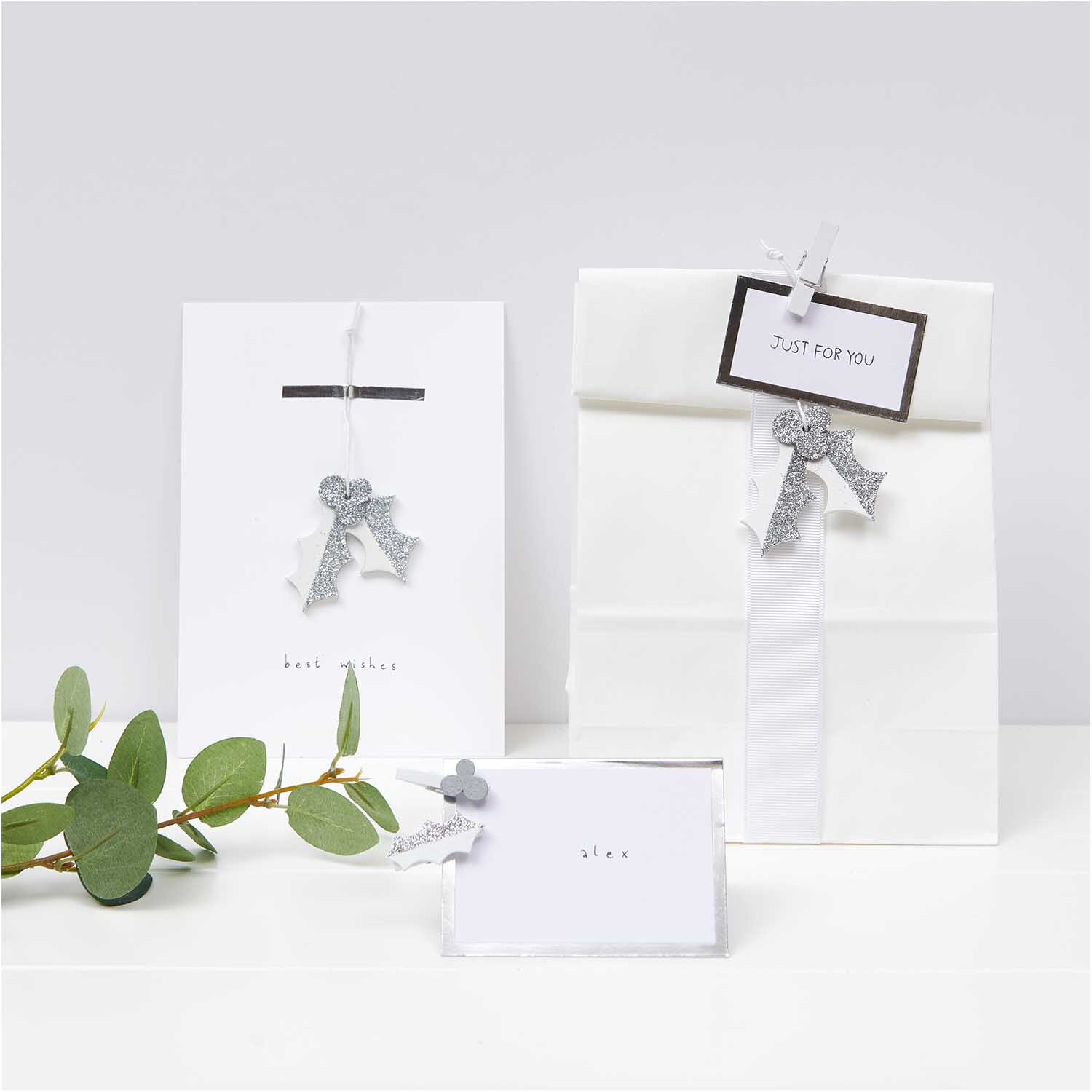 Holzhänger Ilex mit Glitter in elegantem Weiß von Rico Design, dekorativ an Geschenken befestigt.