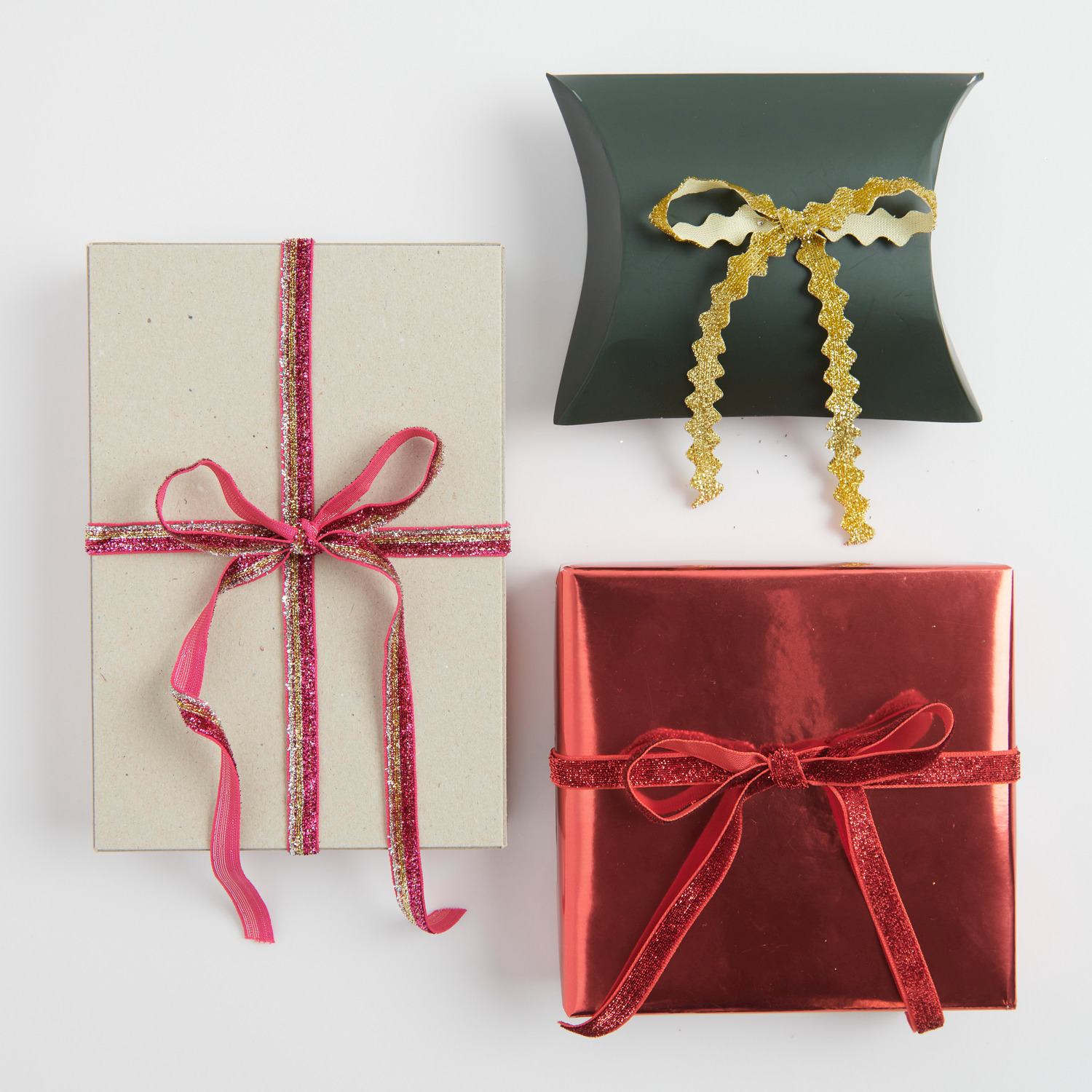 Glitzerband Pink/Gold/Silber: Drei Geschenke mit glänzenden Bändern in Rot und Gold dekoriert.