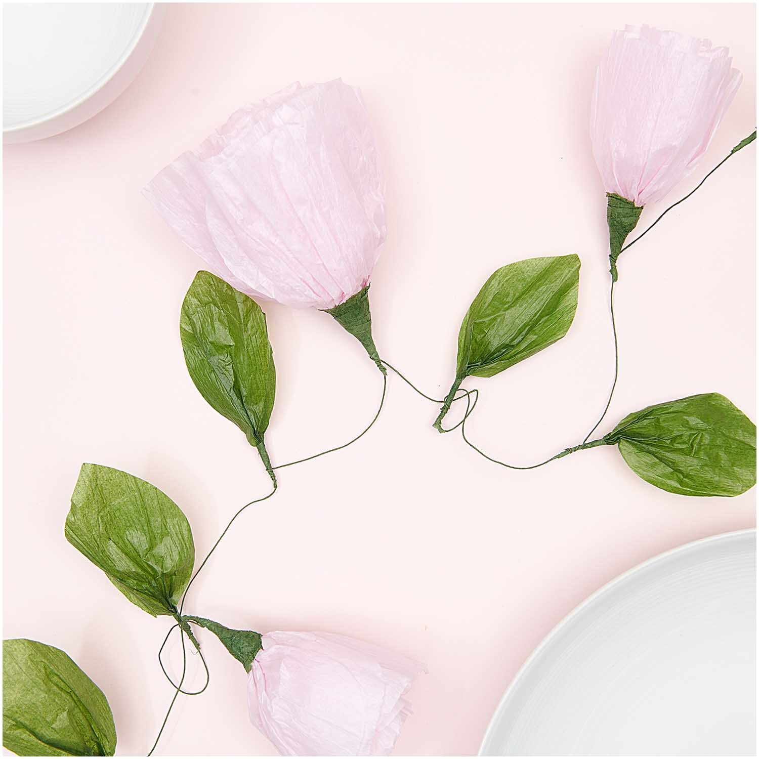 Papierblumen Girlande klein rosa 160 cm von Rico Design, dekorativ arrangiert auf hellem Hintergrund mit grünen Blättern.