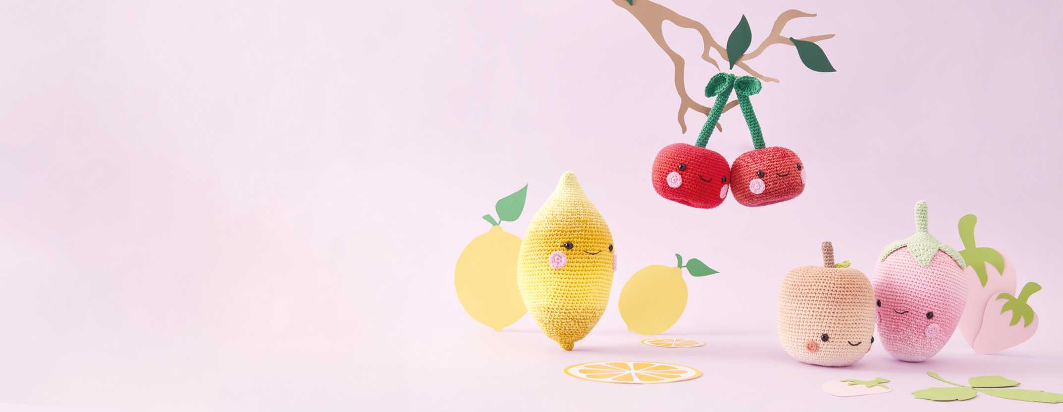 Eine gehäkelte Zitrone, gehäkelte Kirschen, ein gehäkelter Apfel und eine gehäkelte Erdbeere mit lächelnden Gesichtern. Ricorumi Häkelfiguren.