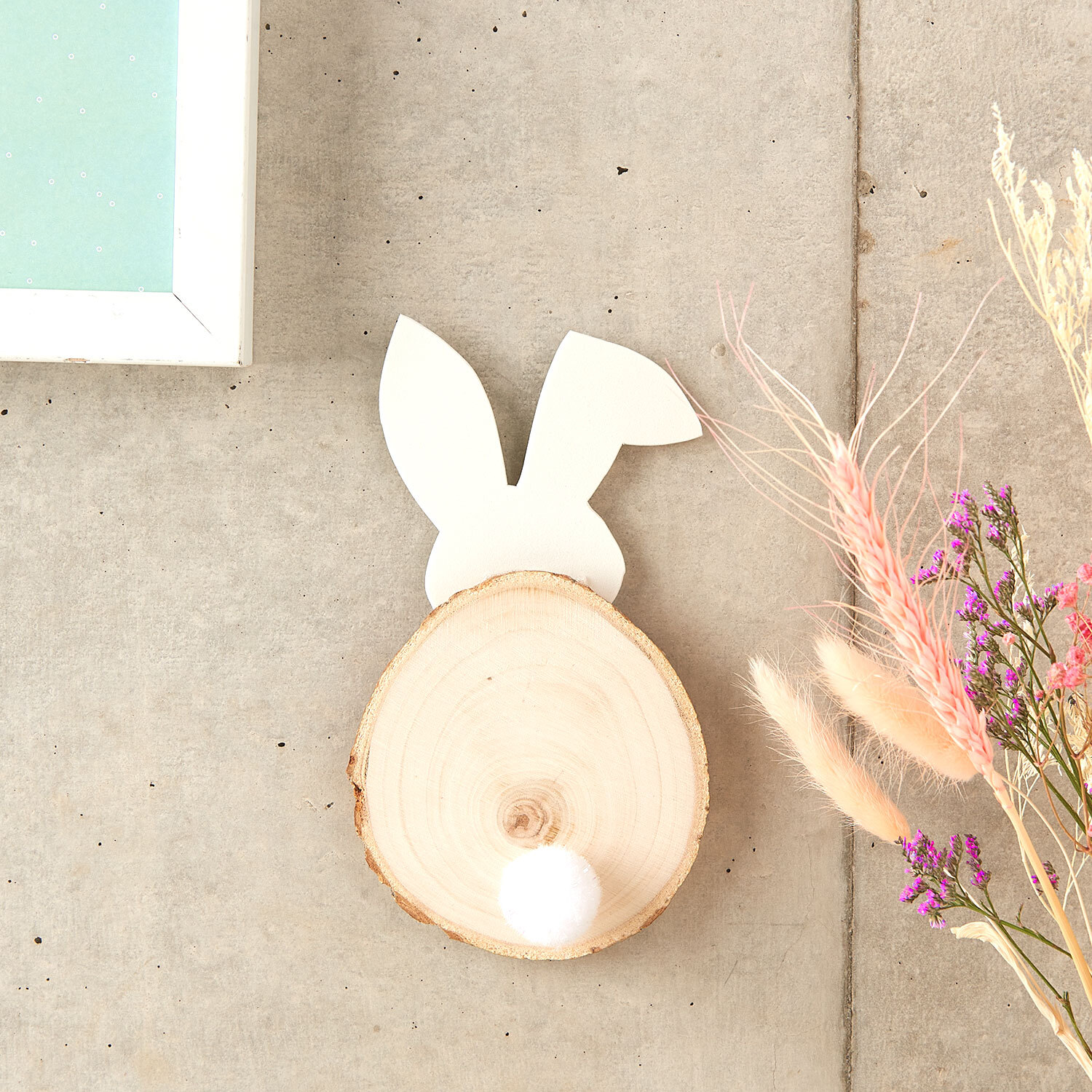 Bastelanleitung Osterhase mit Holzscheibe: DIY-Deko mit Holzscheibe, Hasenohren und Pompon auf Betonhintergrund.