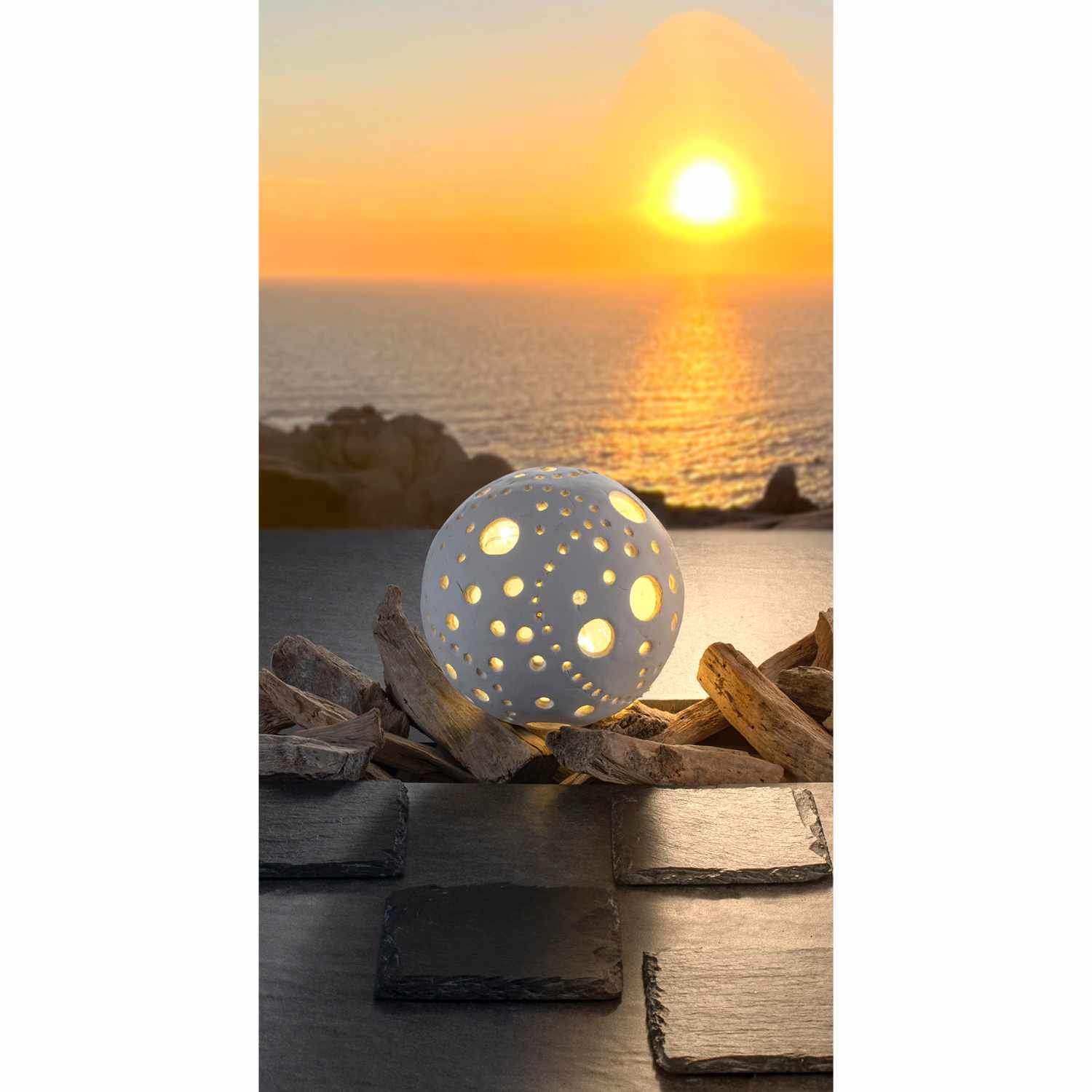 Keramin hellweiß 1000g: Eine weiße, perforierte Kugel von Glorex leuchtet vor einem Sonnenuntergang am Meer.