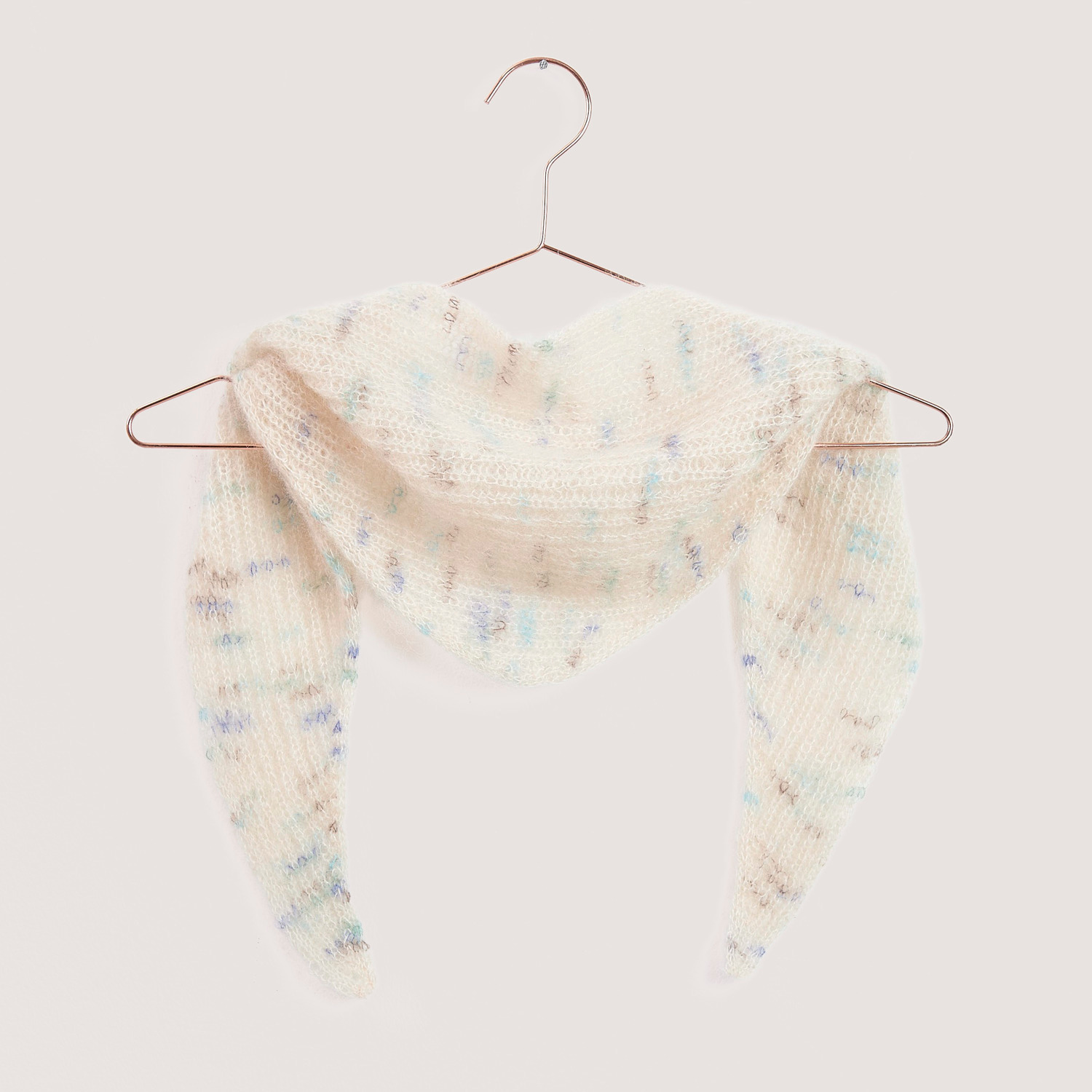 Strickset Mini Dreieckstuch Modell 08b in sanften Pastelltönen, aufgehängt an einem Kleiderbügel.