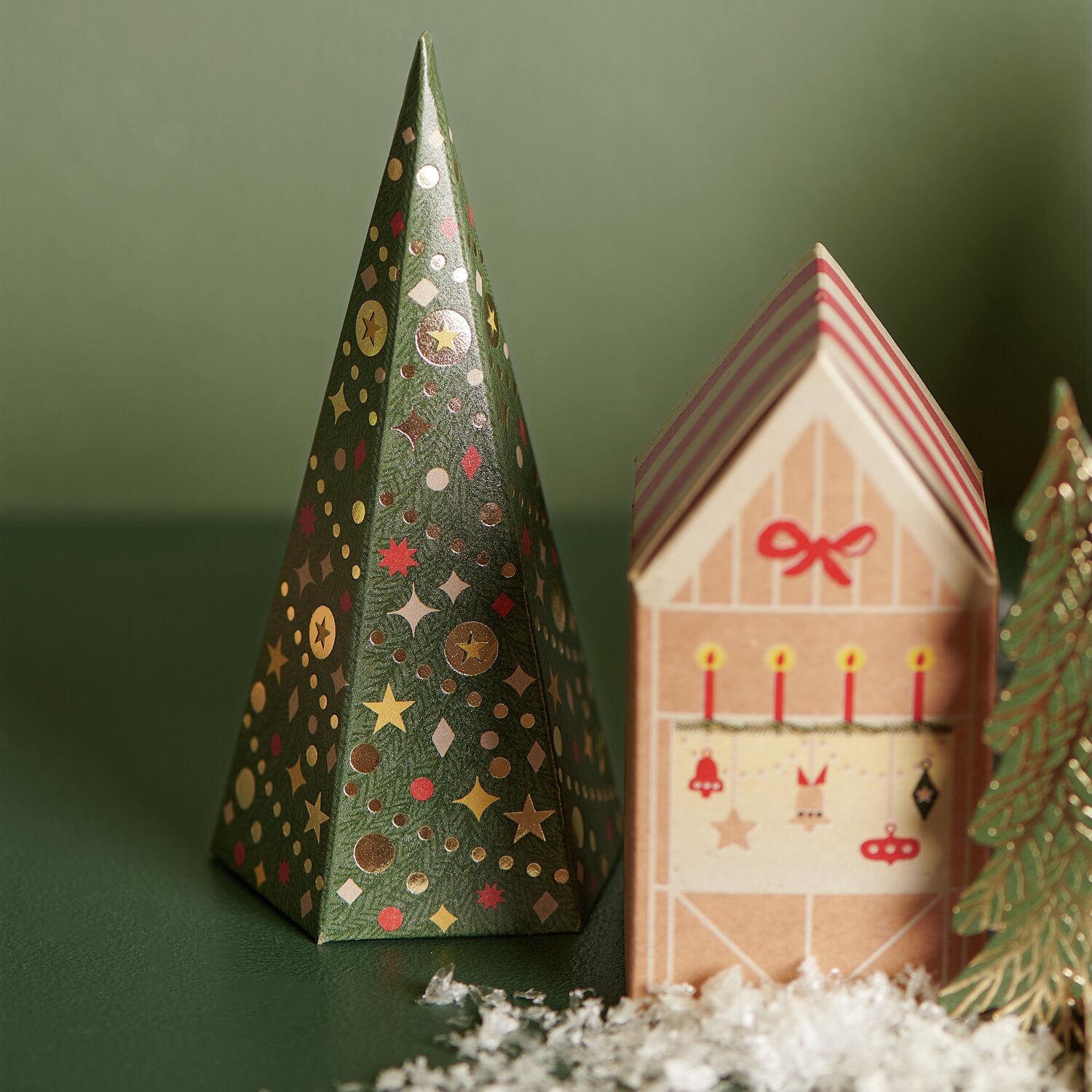 Adventskalender Bastelset: Grüner, festlich verzierter Tannenbaum neben einem dekorativen Haus.