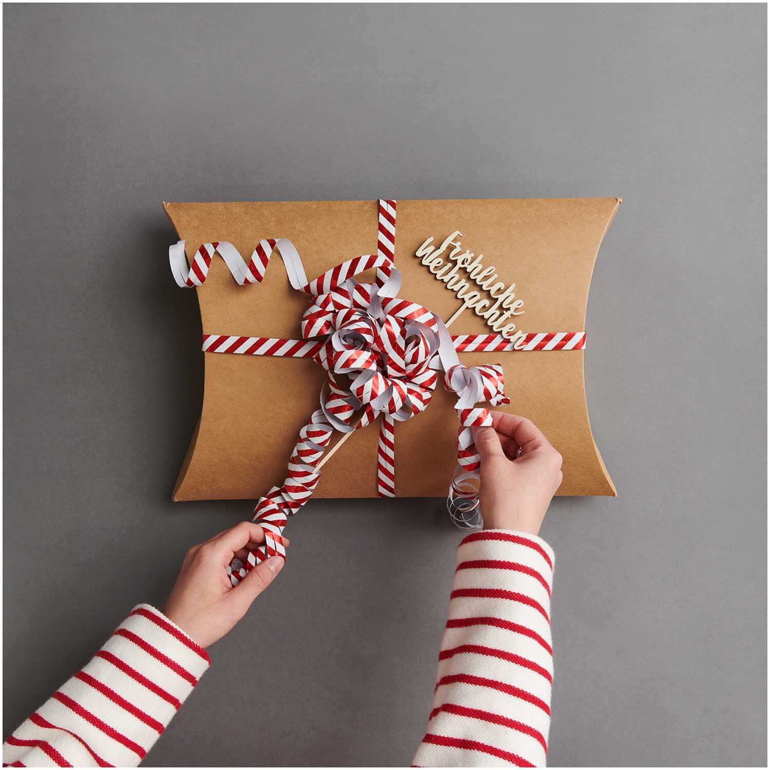 Luftschlangen Streifen rot-weiß 3,8m: Geschenkverpackung mit rot-weißen Streifen und Schleife. Hände binden dekorative Schleife.