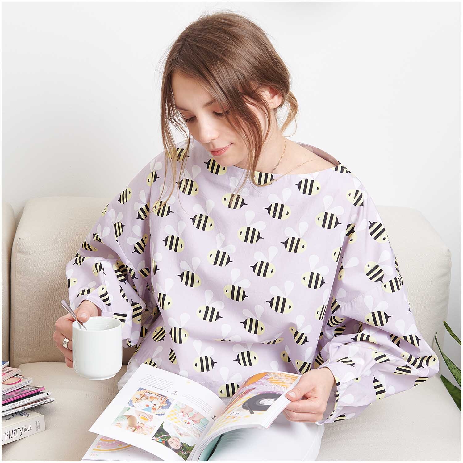 Meterware Baumwoll-Popelin flieder Bienen von Rico Design: Frau liest auf Sofa, trägt fliederfarbenes Oberteil mit Bienenmuster.