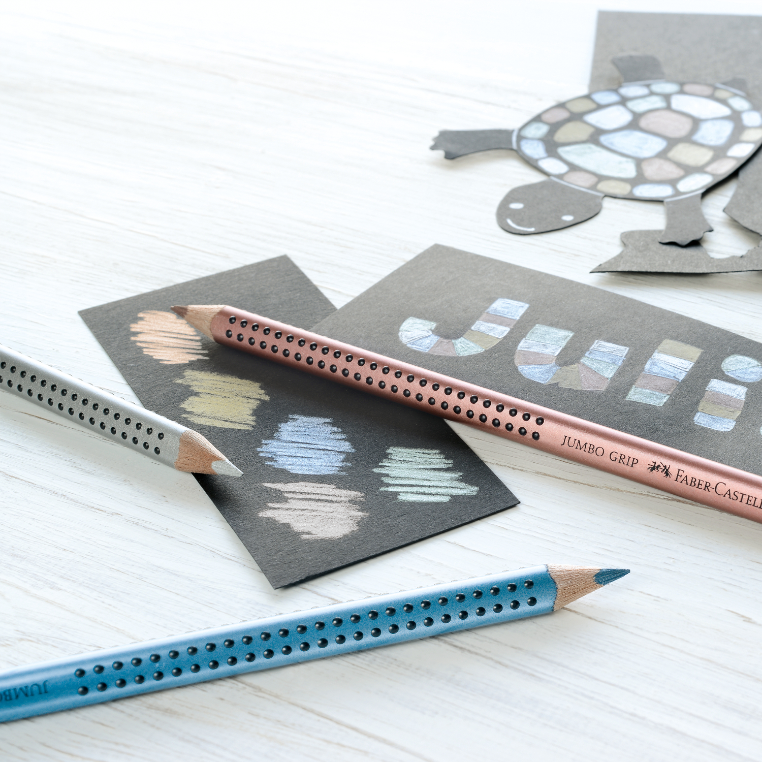 Jumbo Grip metallic Bleistifte von Faber Castell in Blau und anderen Farben auf weißem Tisch mit Zeichnungen.