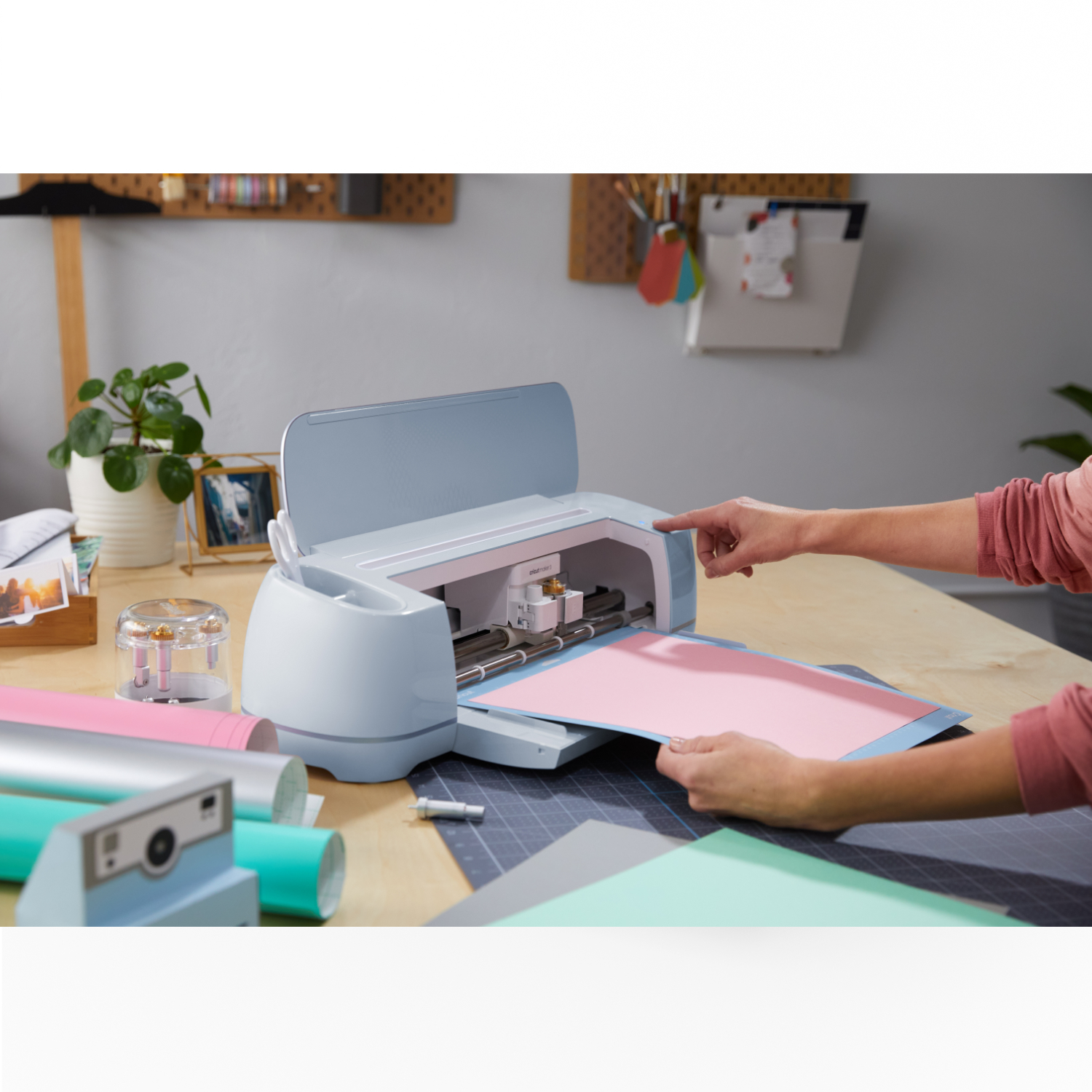 Maker 3 Schneideplotter in Aktion auf einem Tisch, umgeben von buntem Papier und Bastelmaterialien.