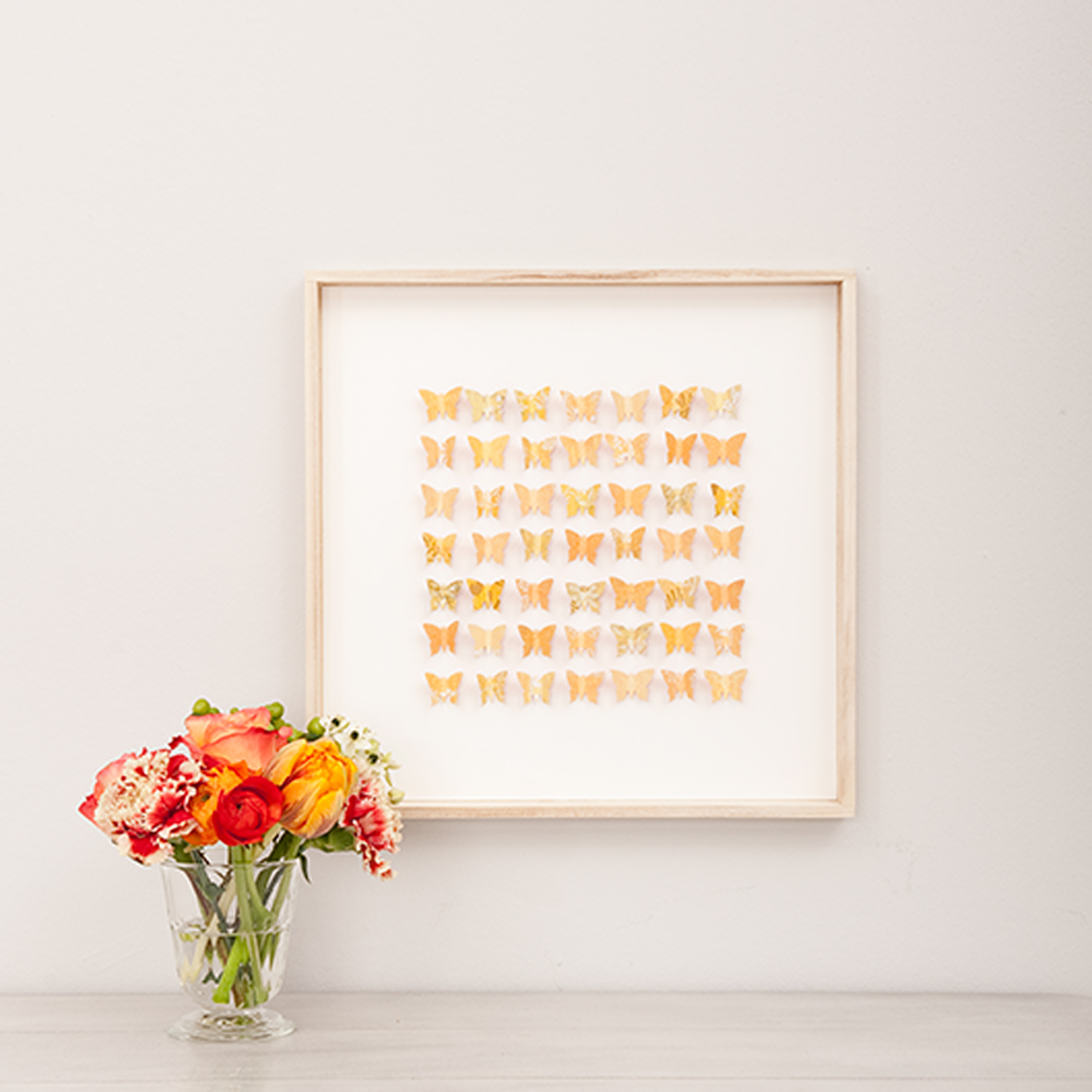 Bastelanleitung 3D-Bilder mit Schmetterlingen: Ein gerahmtes Kunstwerk mit orangefarbenen Schmetterlingen neben einem Blumenstrauß.